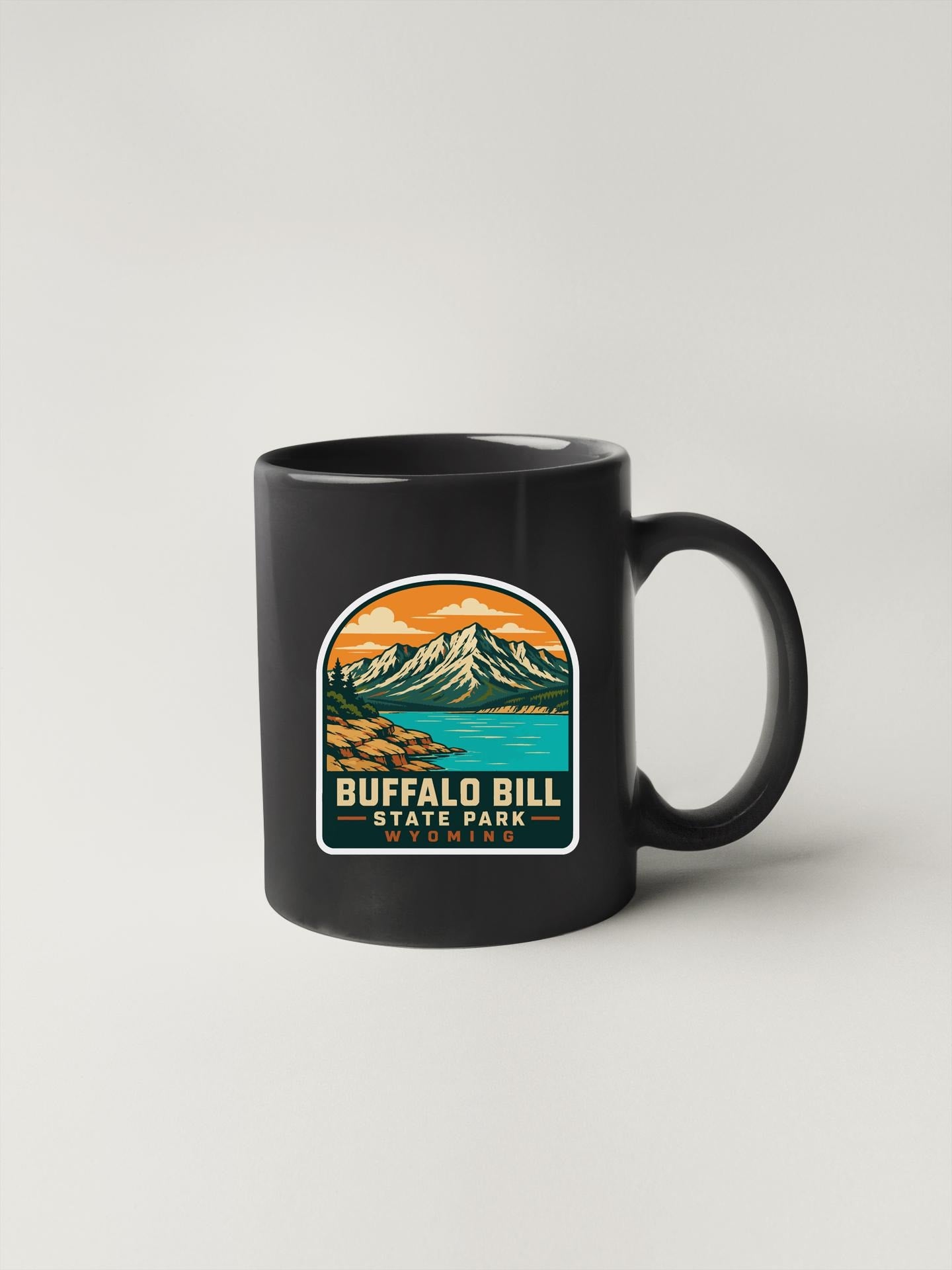 A black coffee mug with a graphic design depicting a mountain landscape and a lake.