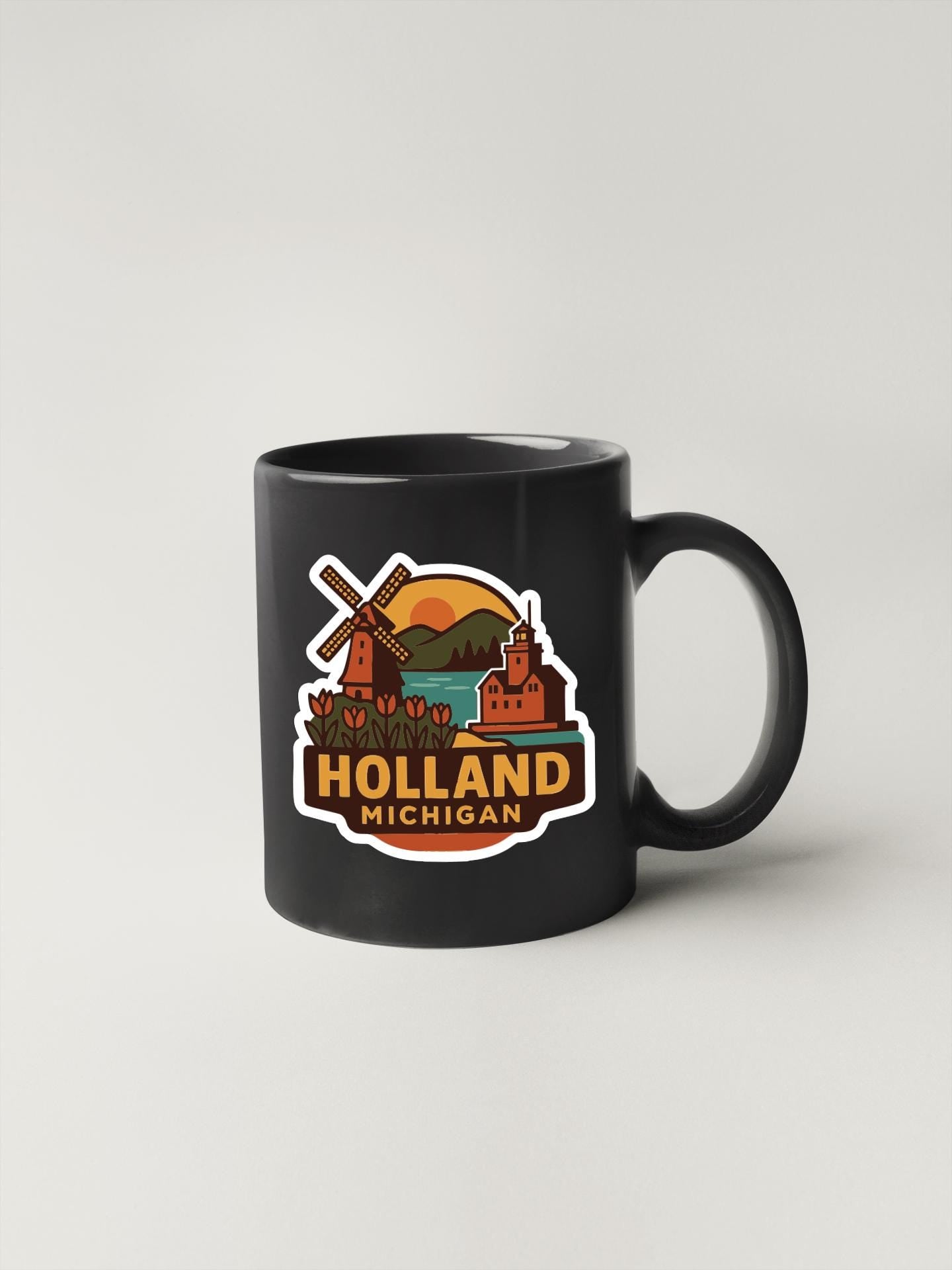 A black coffee mug with a colorful sticker depicting landmarks and scenery from Holland, Michigan.