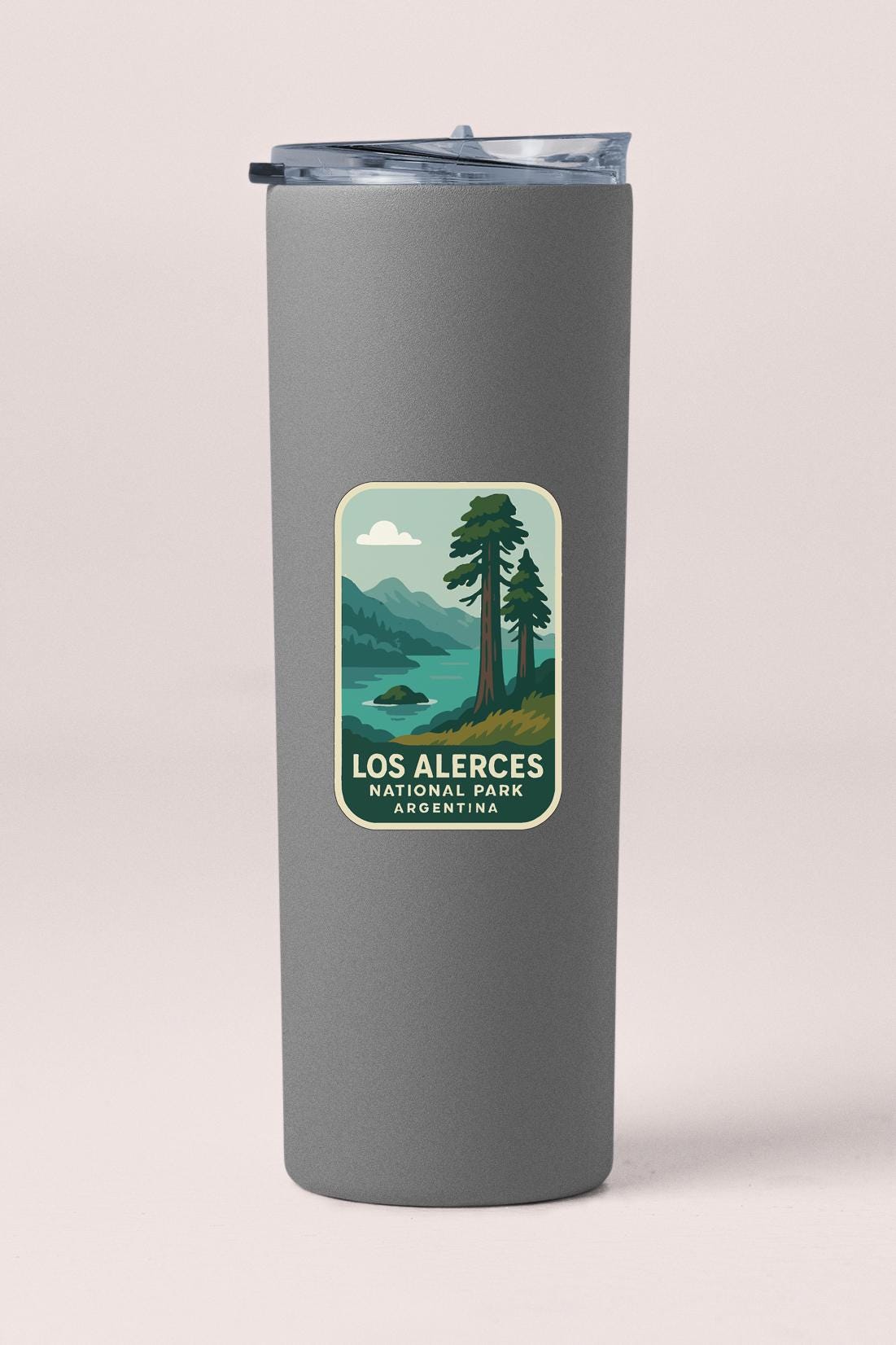 A gray insulated tumbler with a label that features an illustration of a scenic landscape with mountains, trees, and a lake.