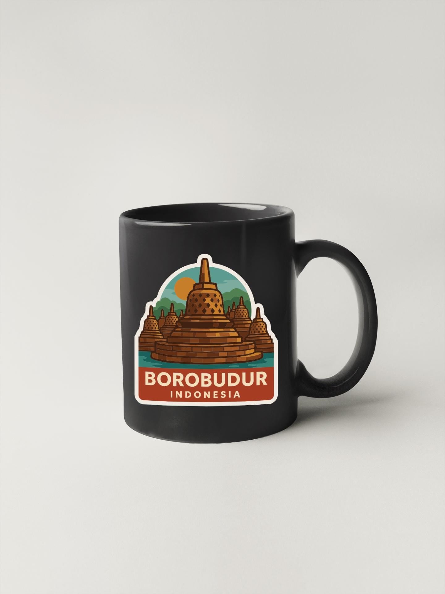 A black coffee mug with a sticker depicting Borobudur, a famous Buddhist temple in Indonesia.