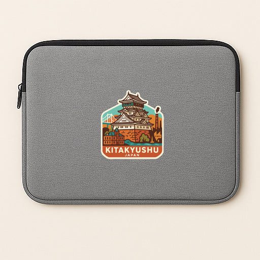 A gray laptop sleeve with a sticker of the castle of Kitakyushu, Japan, printed on it.