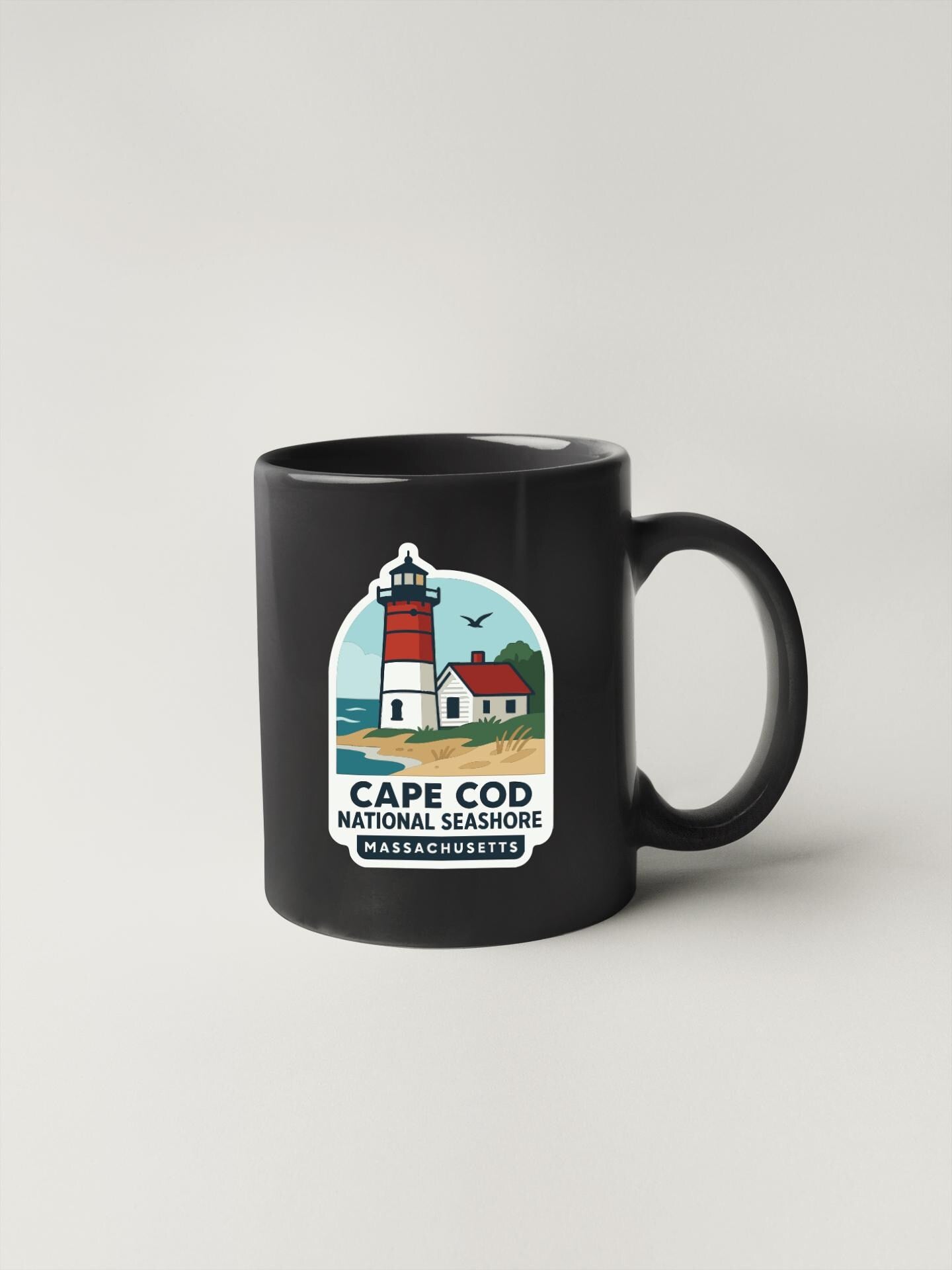 A black coffee mug with a graphic design depicting a lighthouse and a house, along with the text "Cape Cod National Seashore Massachusetts".