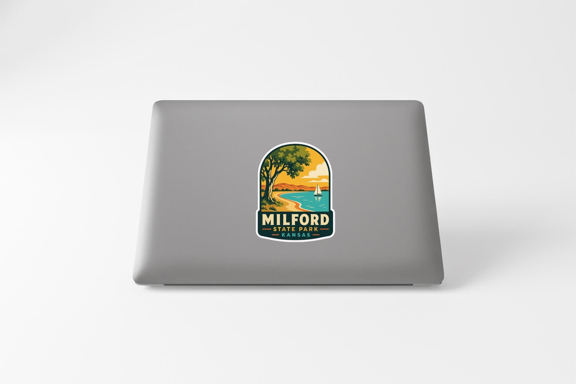 a sticker on the back of a laptop that displays a scenic landscape with a lake, trees, and a sunset.