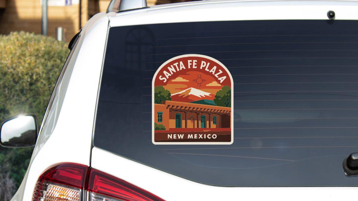 A sticker on the rear window of a white car, depicting Santa Fe Plaza in New Mexico.