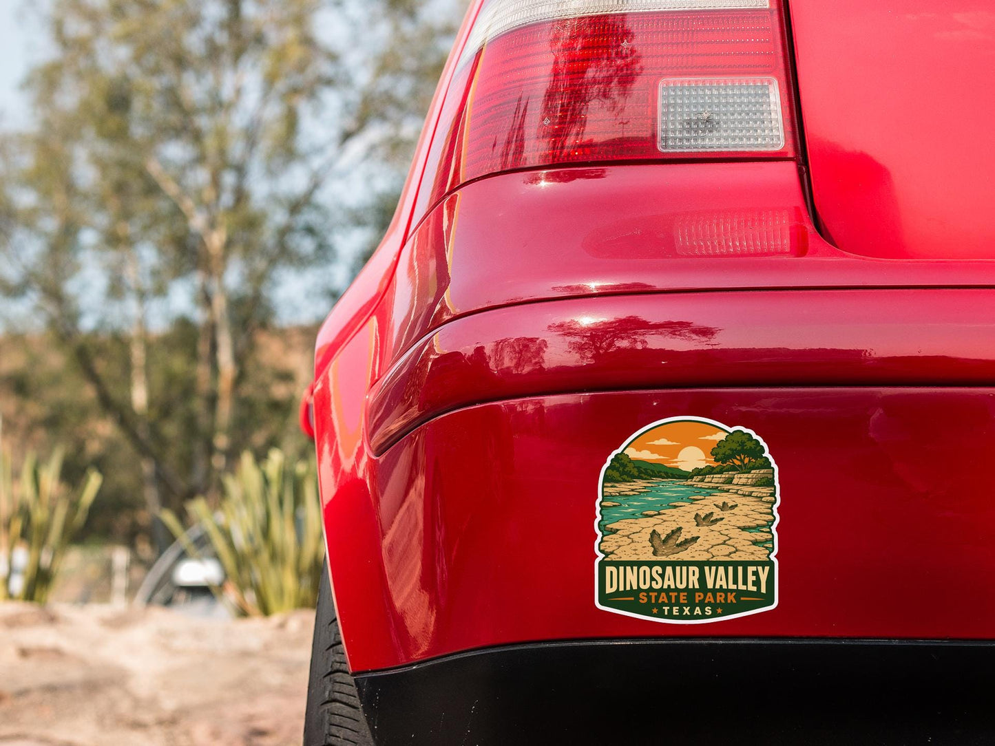 the rear end of a red car with a sticker on the trunk that says "DINOSAUR VALLEY STATE PARK TEXAS".