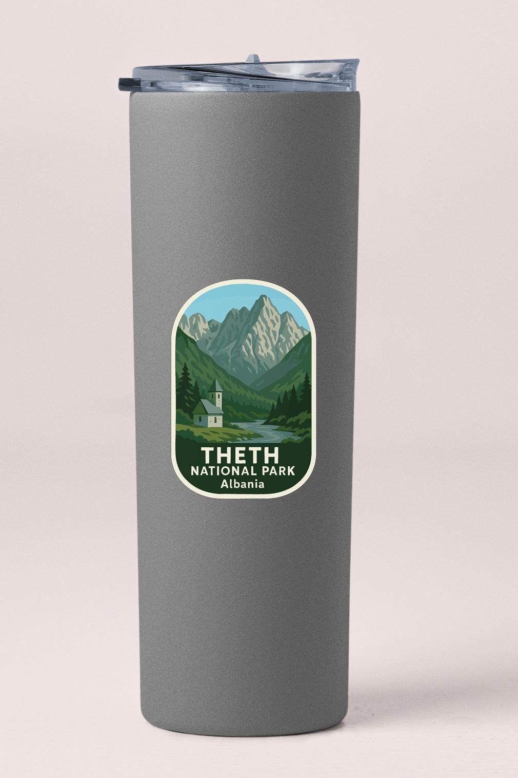 A gray insulated tumbler with a label that features a mountain landscape and the text "THETH NATIONAL PARK ALBANIA".