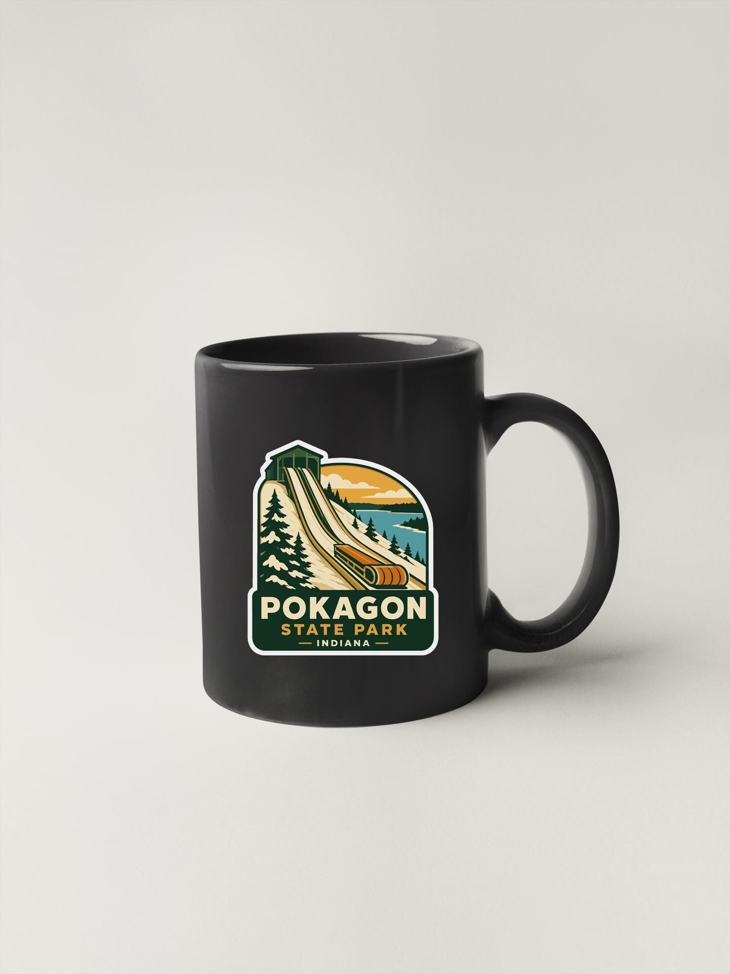 A black coffee mug with a sticker depicting a scenic landscape, including a mountain, trees, and a body of water.