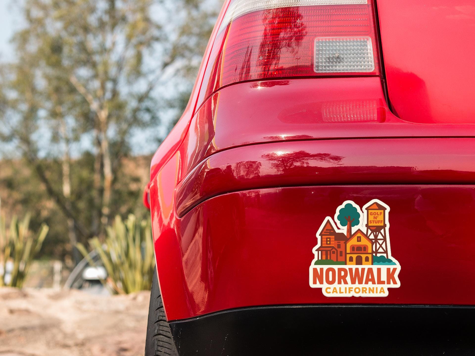 the rear end of a red car with a sticker on the trunk that says "NORWALK CALIFORNIA".