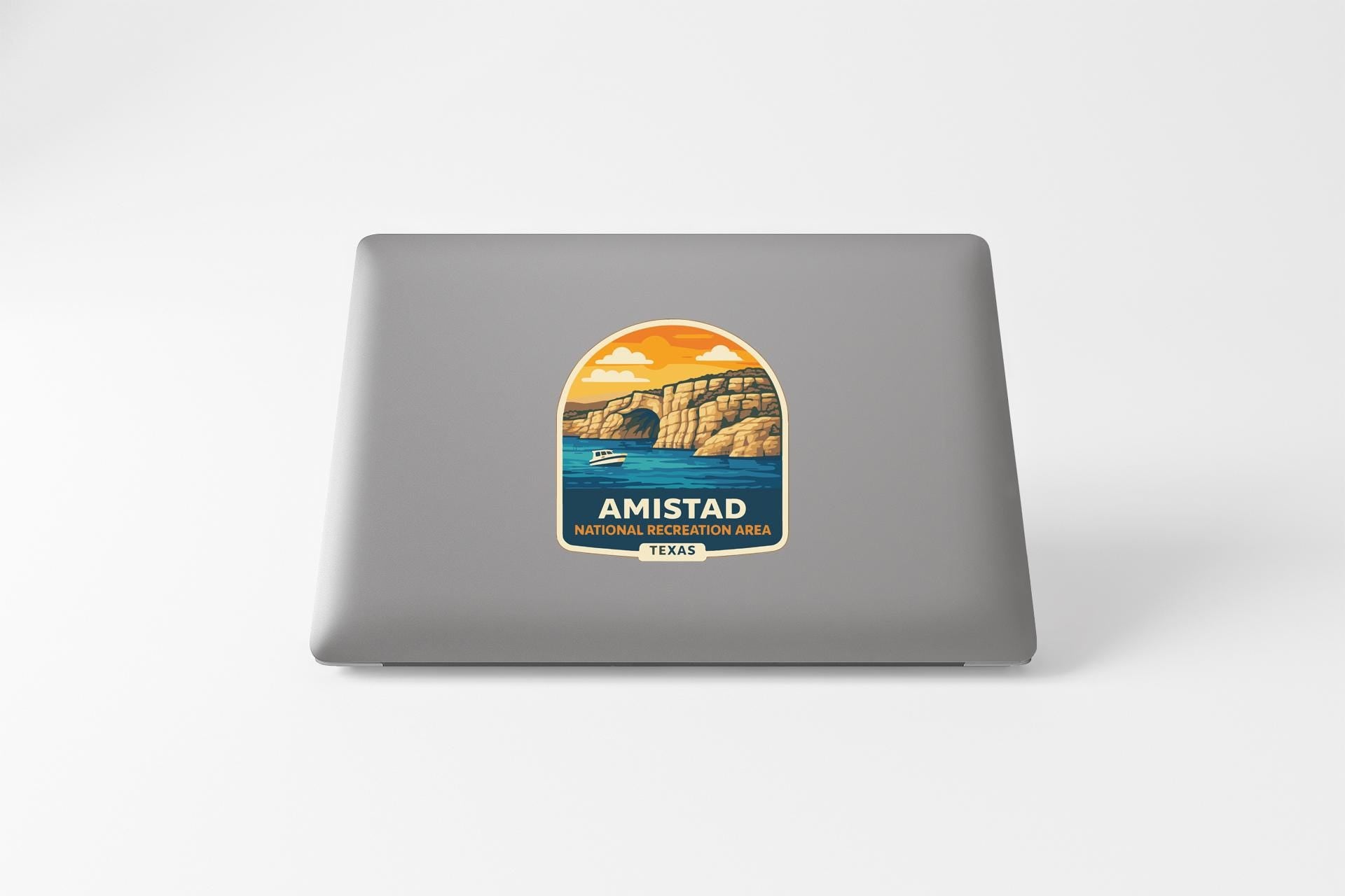 a sticker or decal on the back of a laptop, depicting a scenic landscape with a lake, mountains, and a sunset.
