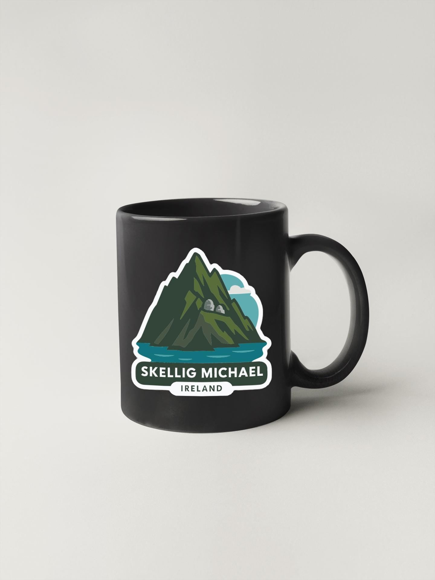 A black coffee mug with a graphic design depicting a mountain and a lake, along with the text "SKELLIG MICHAEL IRELAND".