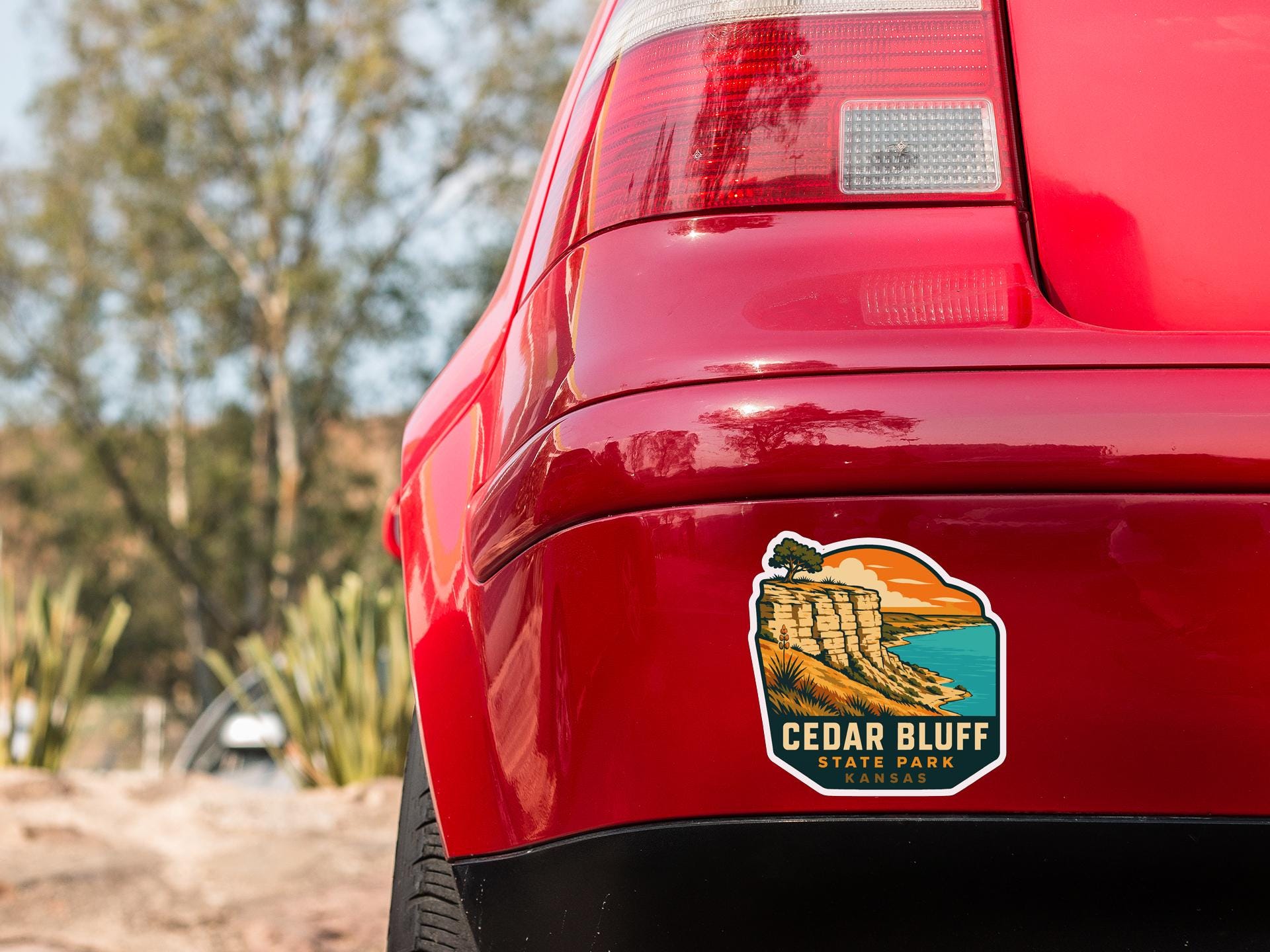 the rear end of a red car with a sticker on the back window that says "Cedar Bluff State Park Kansas".