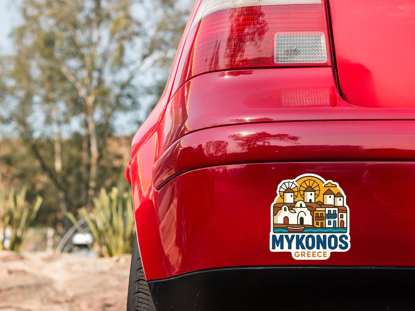 the rear end of a red car with a sticker on it, featuring a stylized illustration of a Greek town.