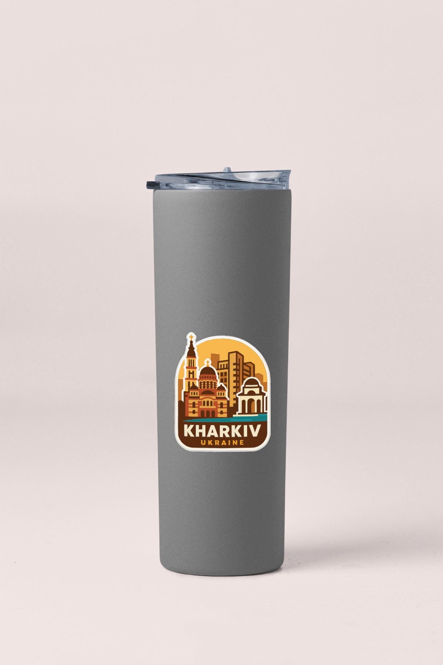 A gray insulated tumbler with a sticker depicting the Kharkiv, Ukraine skyline.