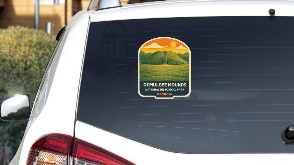 A sticker on the rear window of a white car, depicting a scenic landscape with mountains and a sunset.
