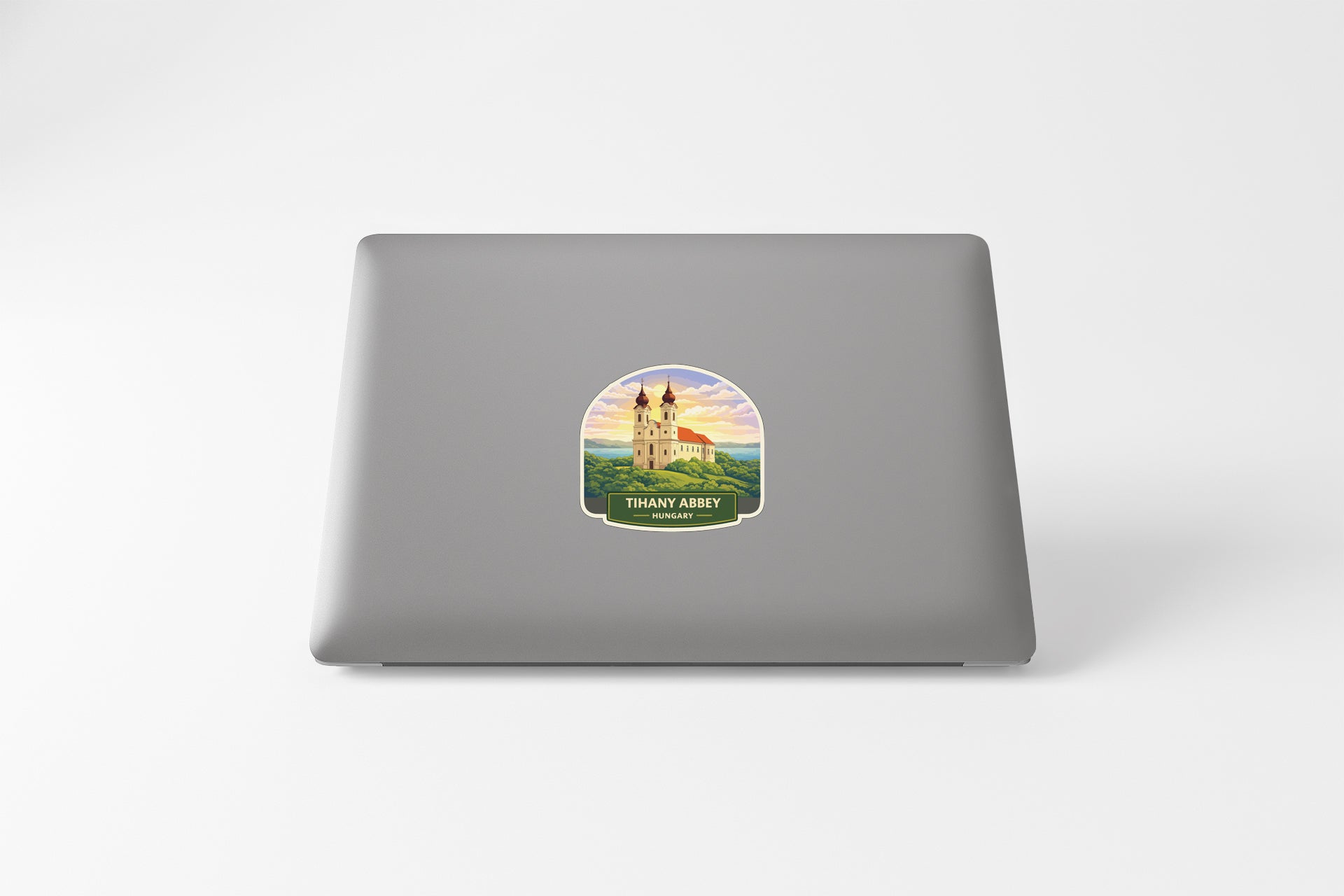 A sticker depicting a castle on a hill with a sunset in the background is placed on the back of a laptop computer.