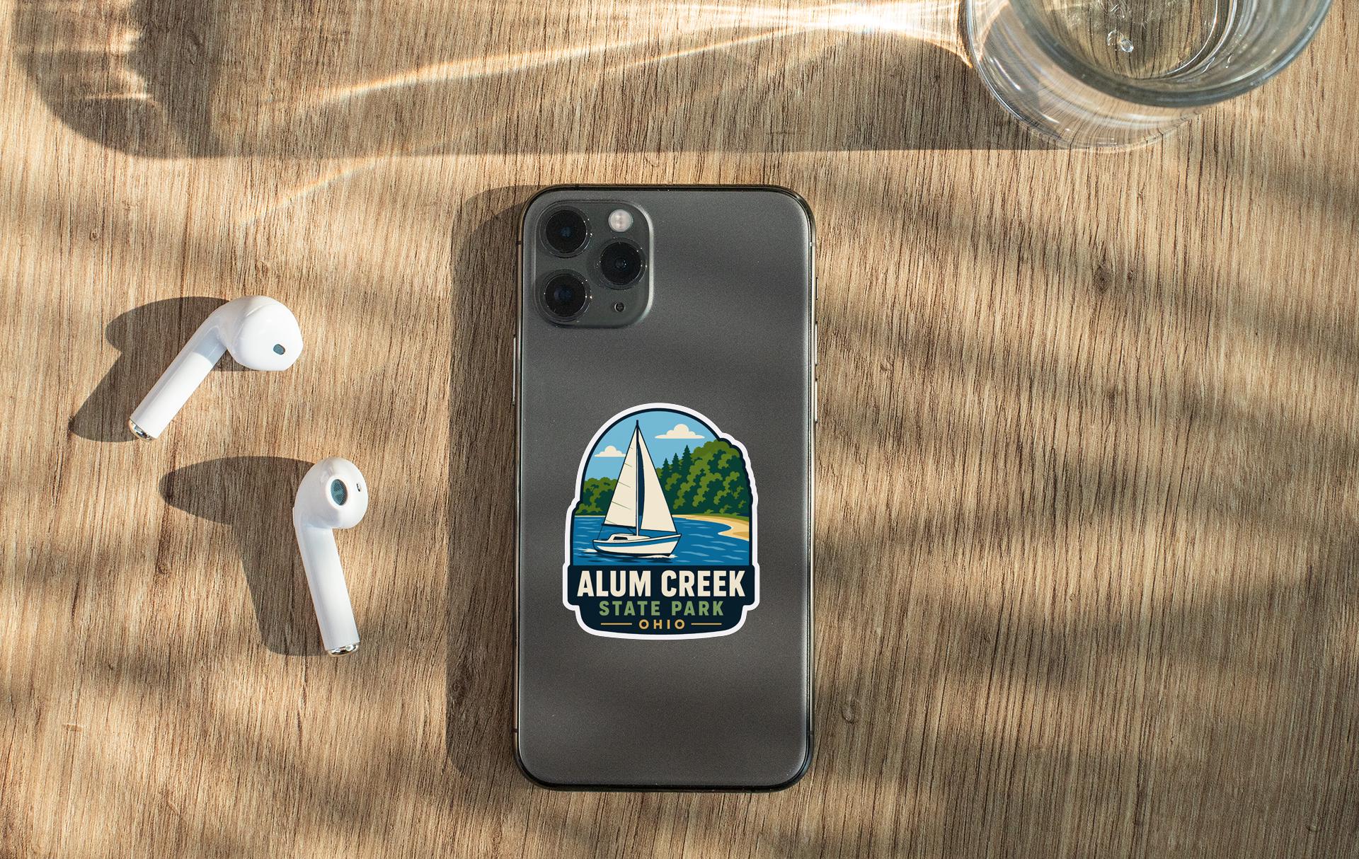 a smartphone with a sticker on it, placed on a wooden surface alongside a pair of white earbuds and a glass of water.
