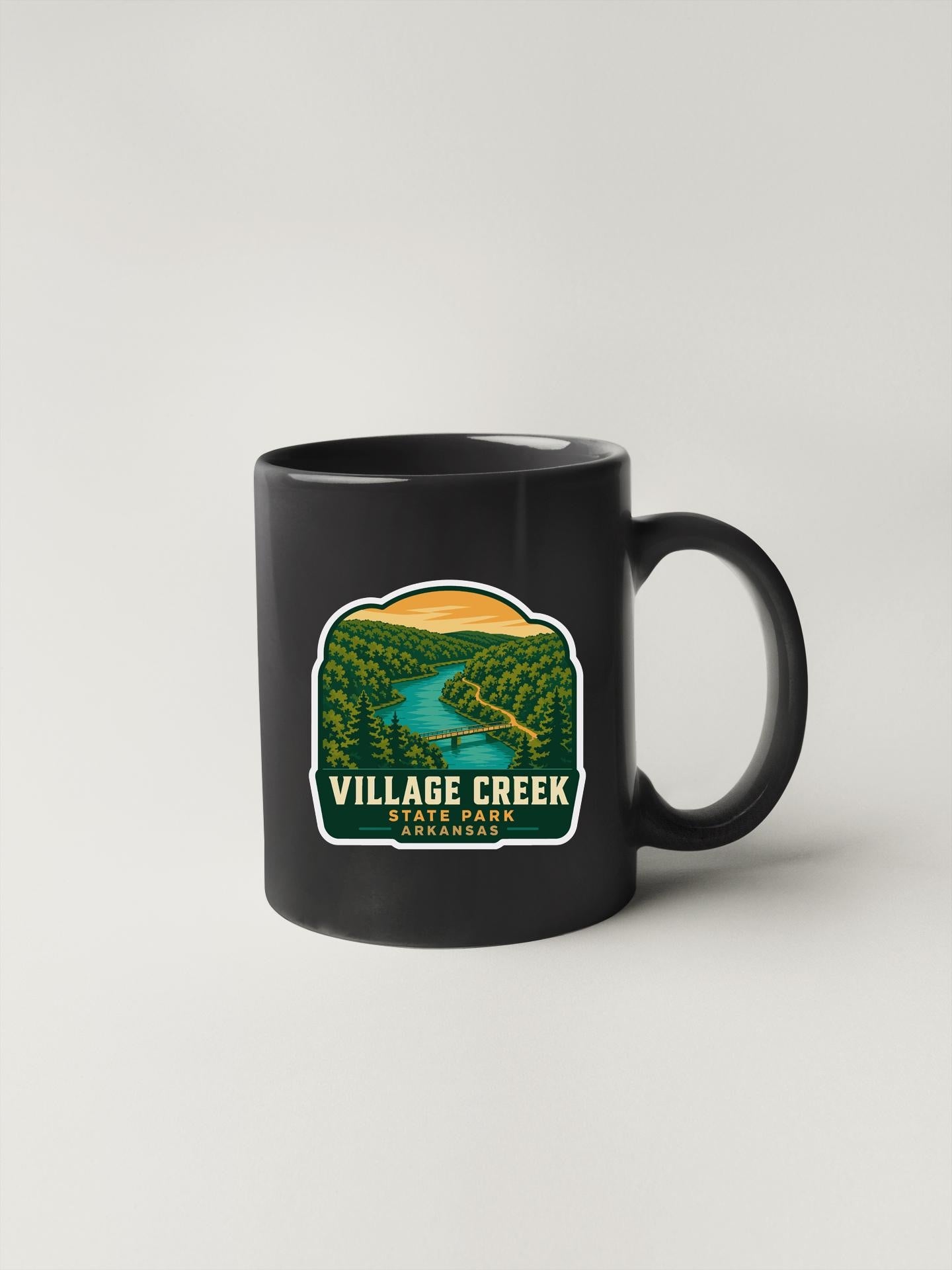 A black coffee mug with a sticker depicting a scenic landscape, including a river and forest.