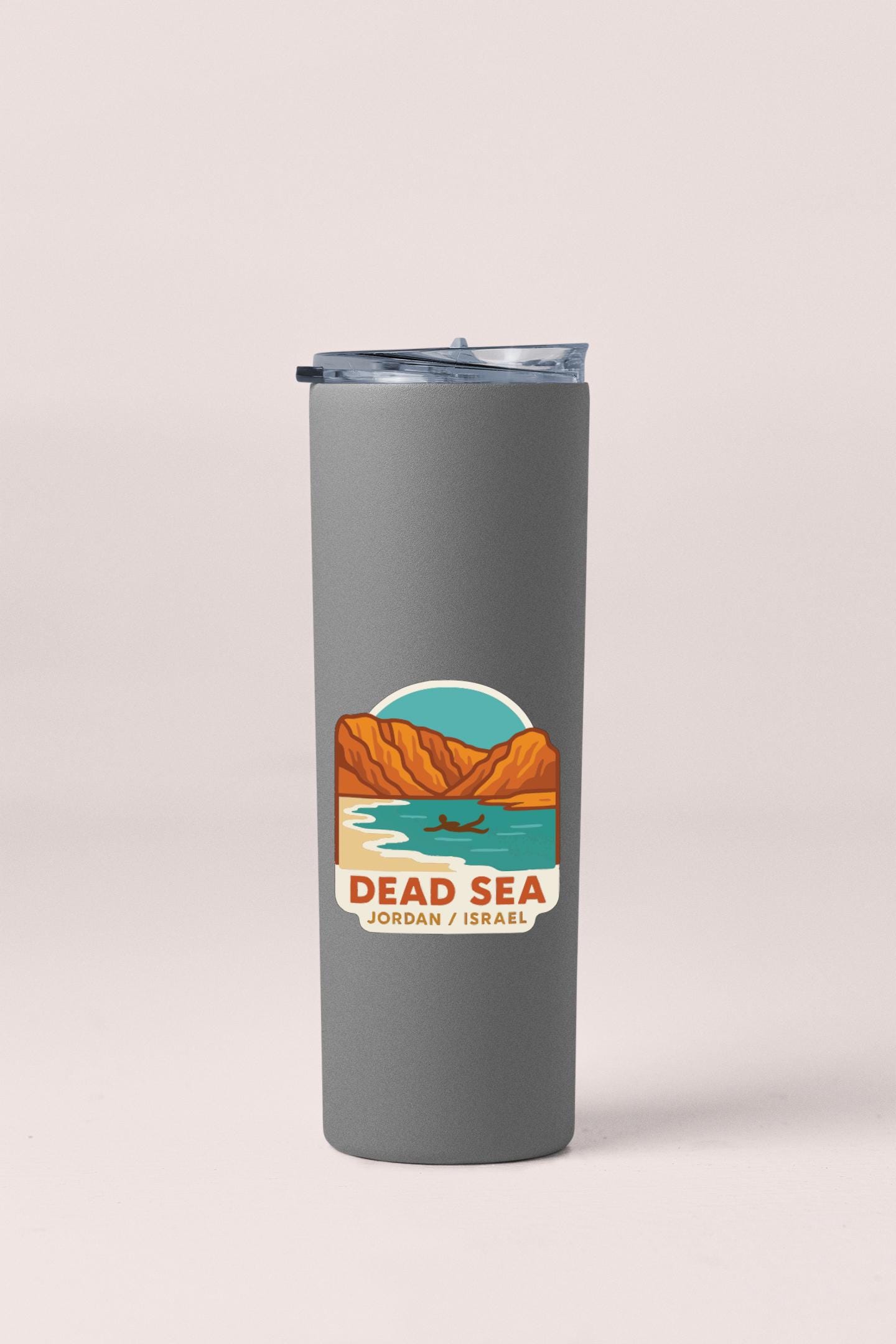 A gray insulated tumbler with a graphic design depicting a desert landscape and a small boat on a body of water.