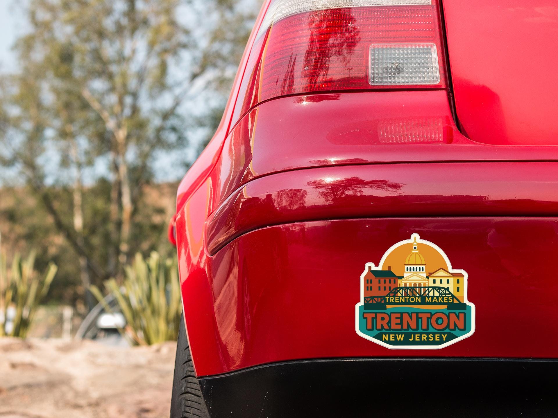 the rear end of a red car with a sticker on it, featuring a cityscape and the text "Trenton, New Jersey".