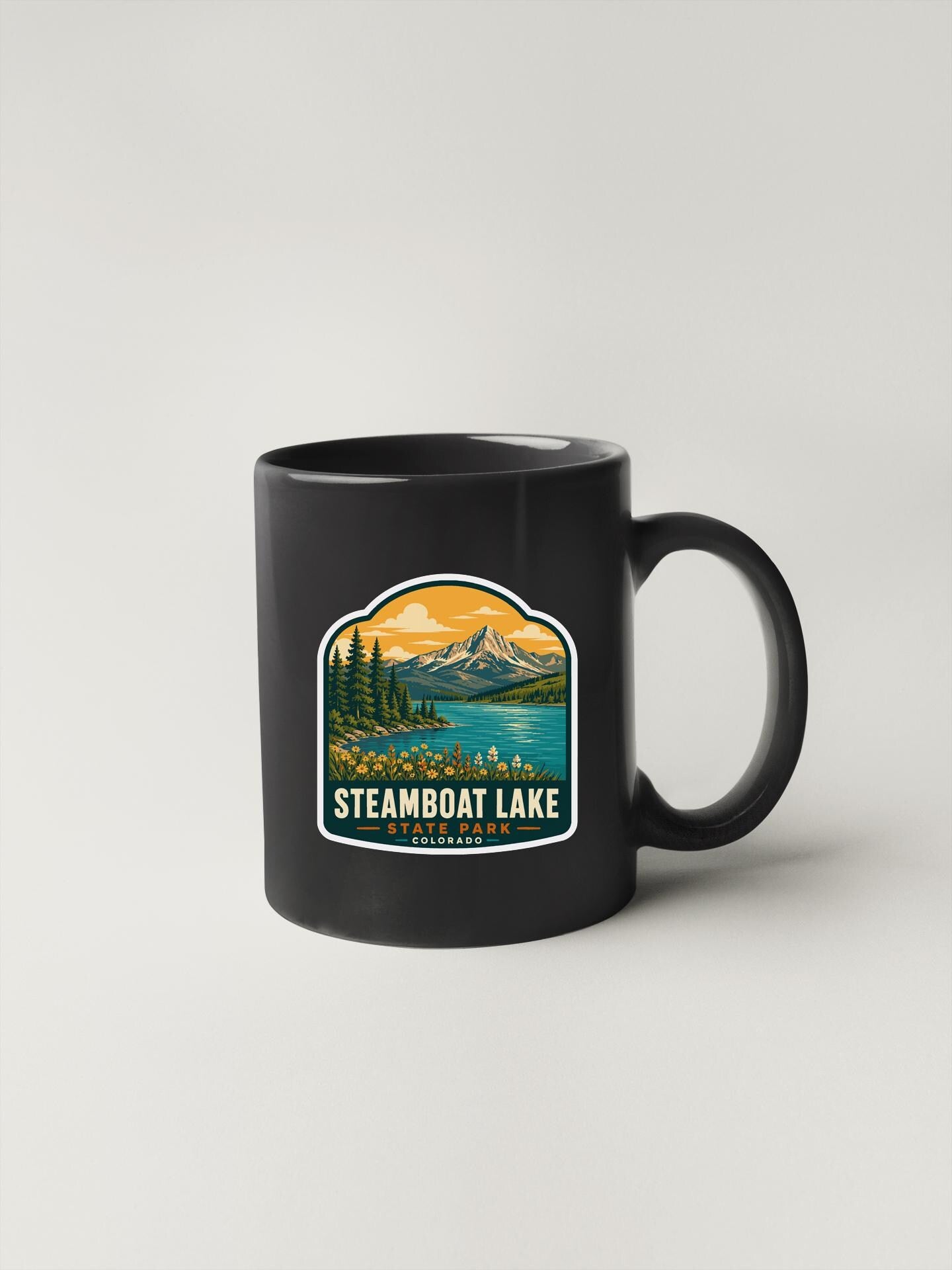 A black coffee mug with a sticker depicting a scenic landscape featuring Steamboat Lake.