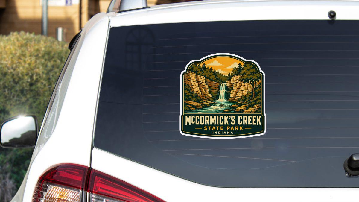 A sticker on the rear window of a white car, depicting a scenic landscape with a waterfall and forest.