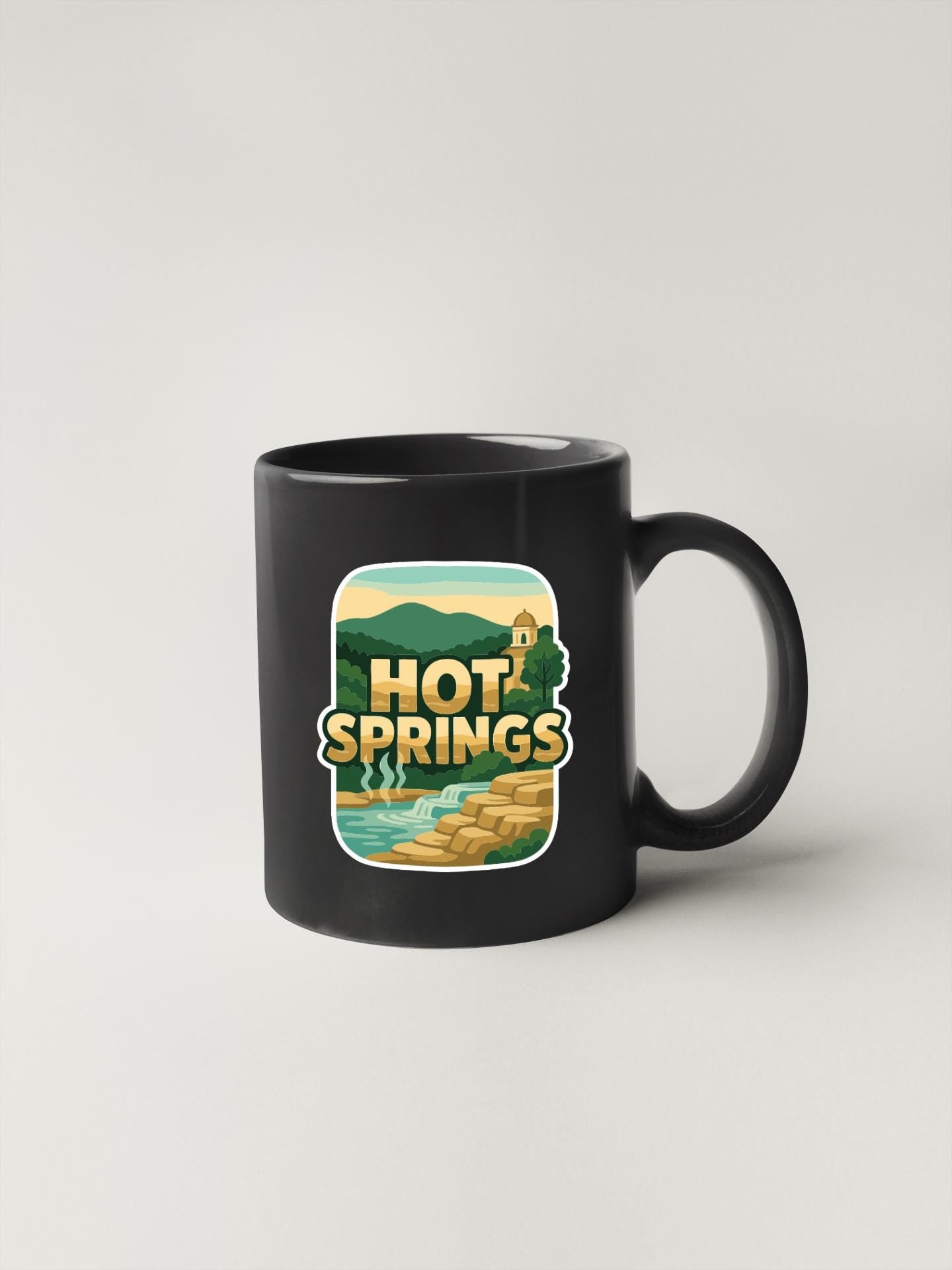A black coffee mug with a graphic design featuring a scenic landscape with mountains, water, and a building.
