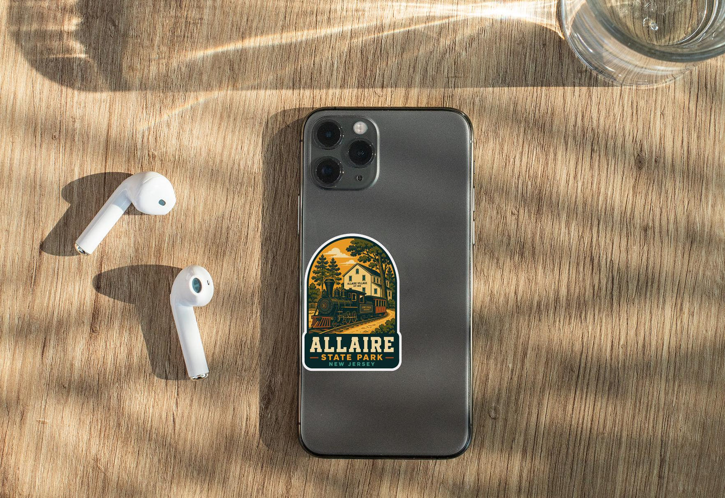 a smartphone with a sticker on it, placed on a wooden surface alongside a pair of white earbuds and a glass of water.