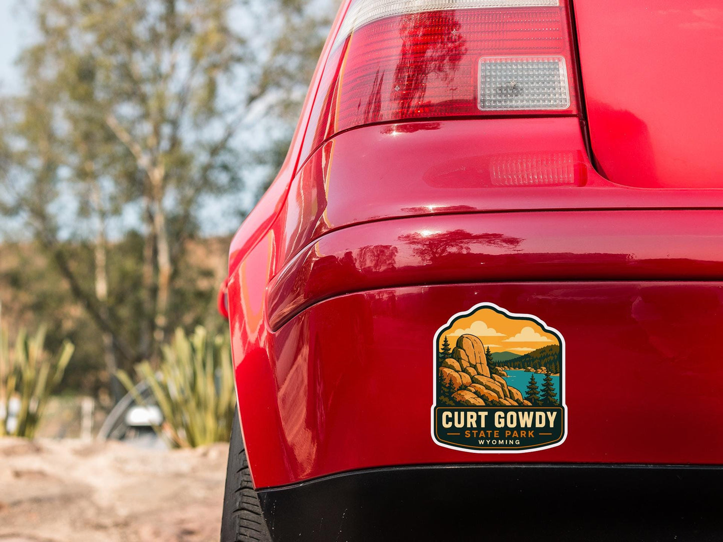 the rear end of a red car with a sticker on the trunk that says "Curt Gowdy State Park, Wyoming".