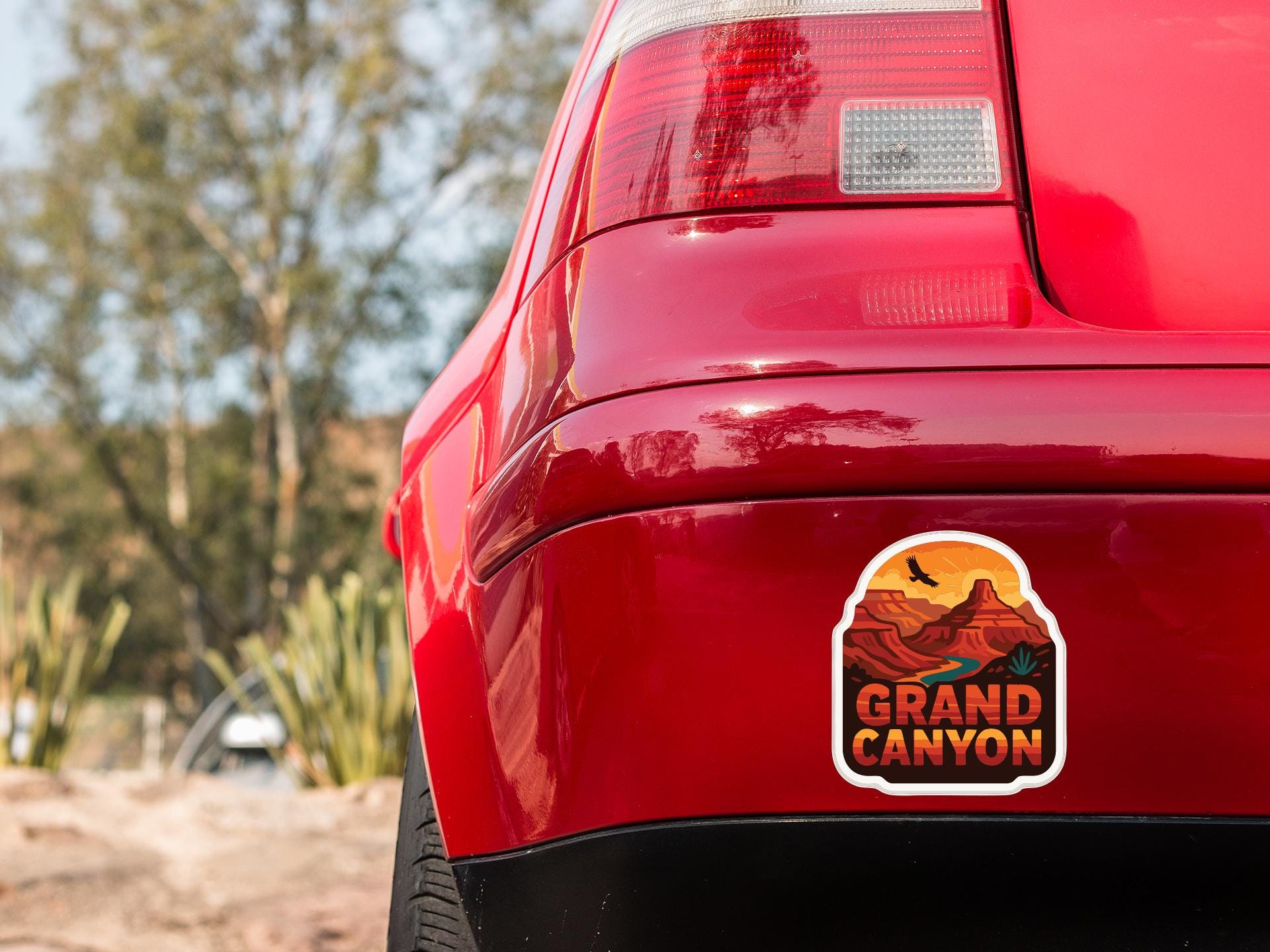 the rear end of a red car with a sticker on the trunk that says "GRAND CANYON".