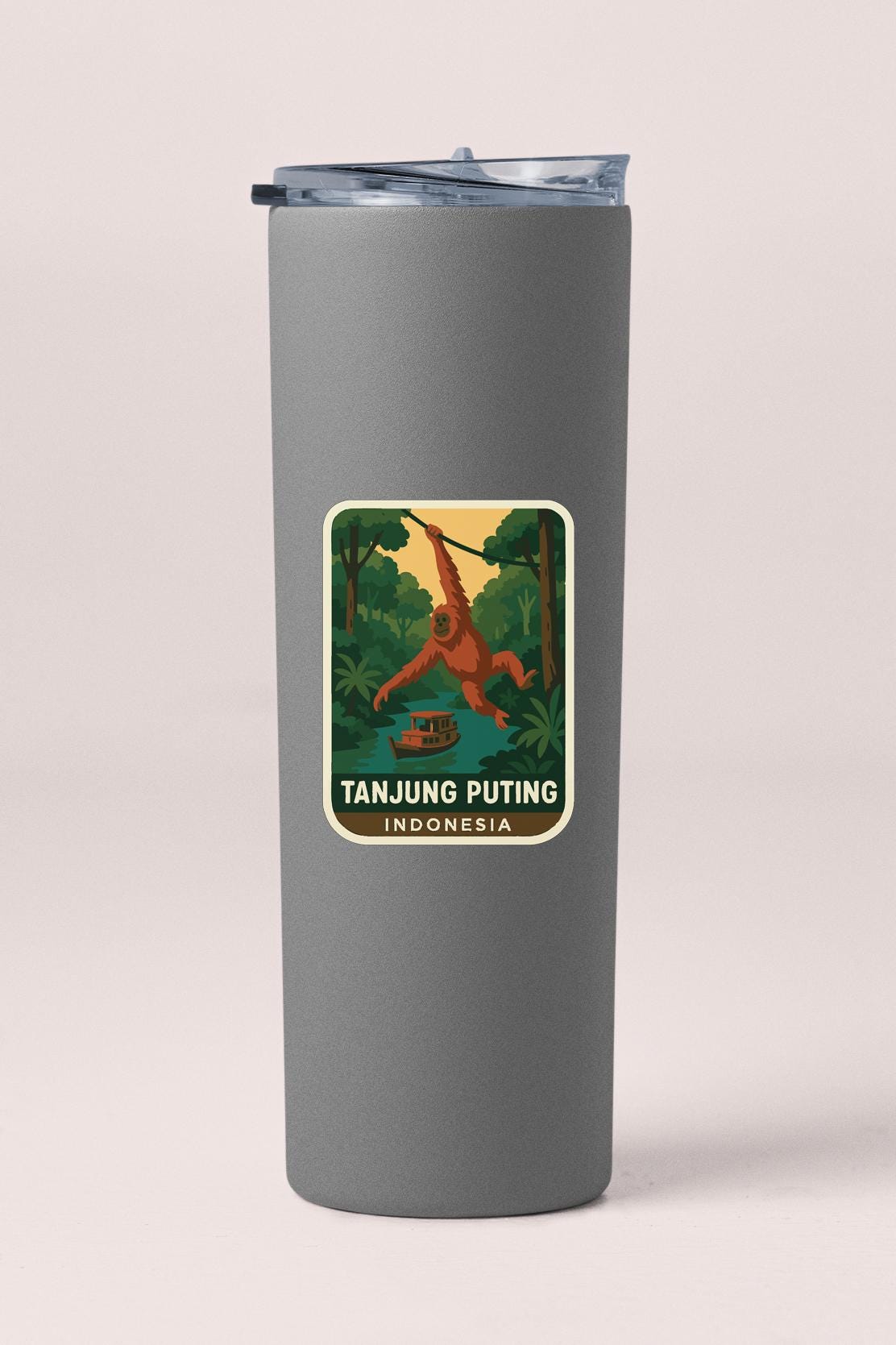 A gray tumbler with a sticker depicting an orangutan in a jungle setting, along with the text "TANJUNG PUTING INDONESIA".