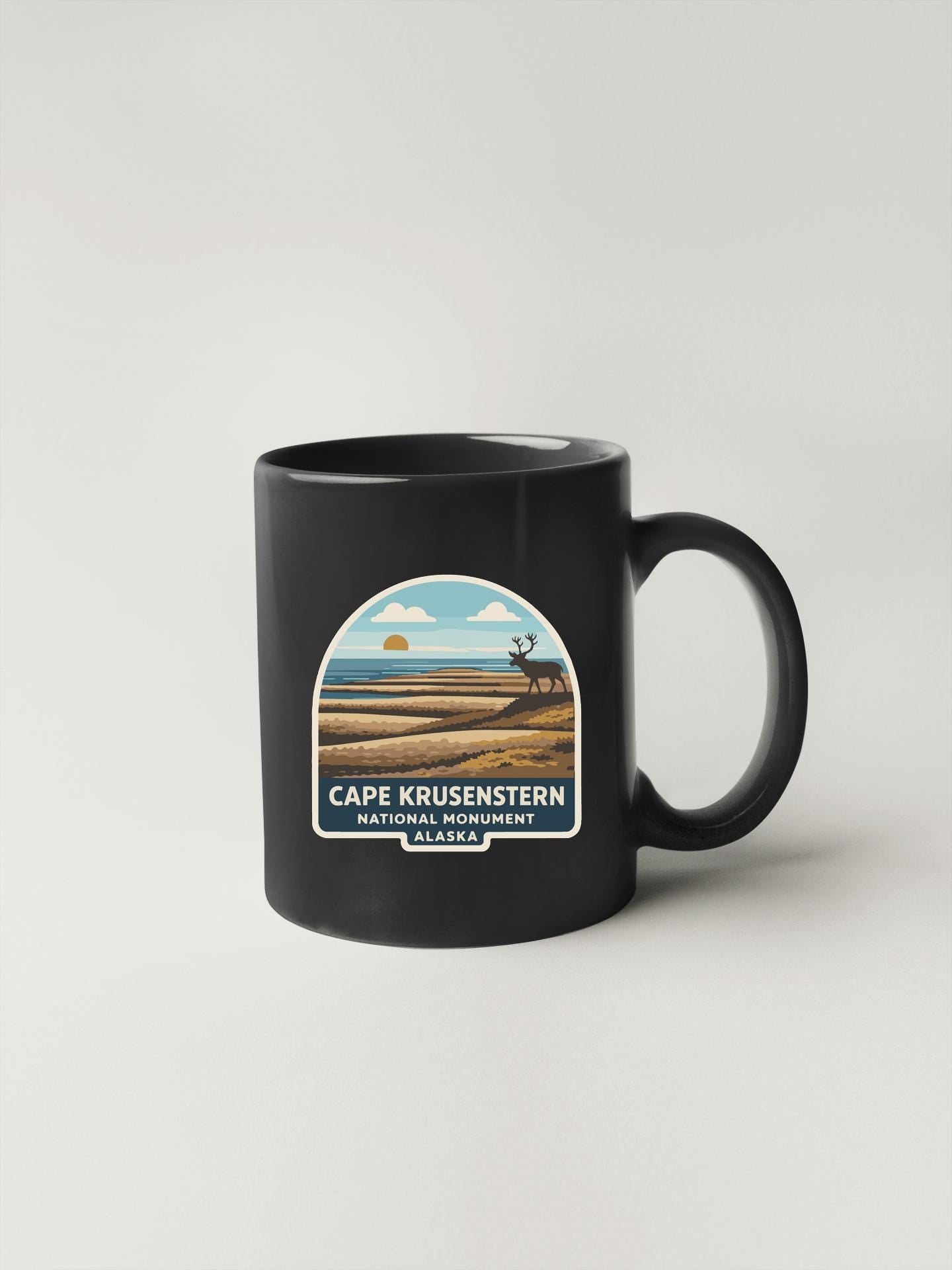 A black coffee mug with a graphic design depicting a scenic landscape featuring a mountain range, a lake, and a sunset.