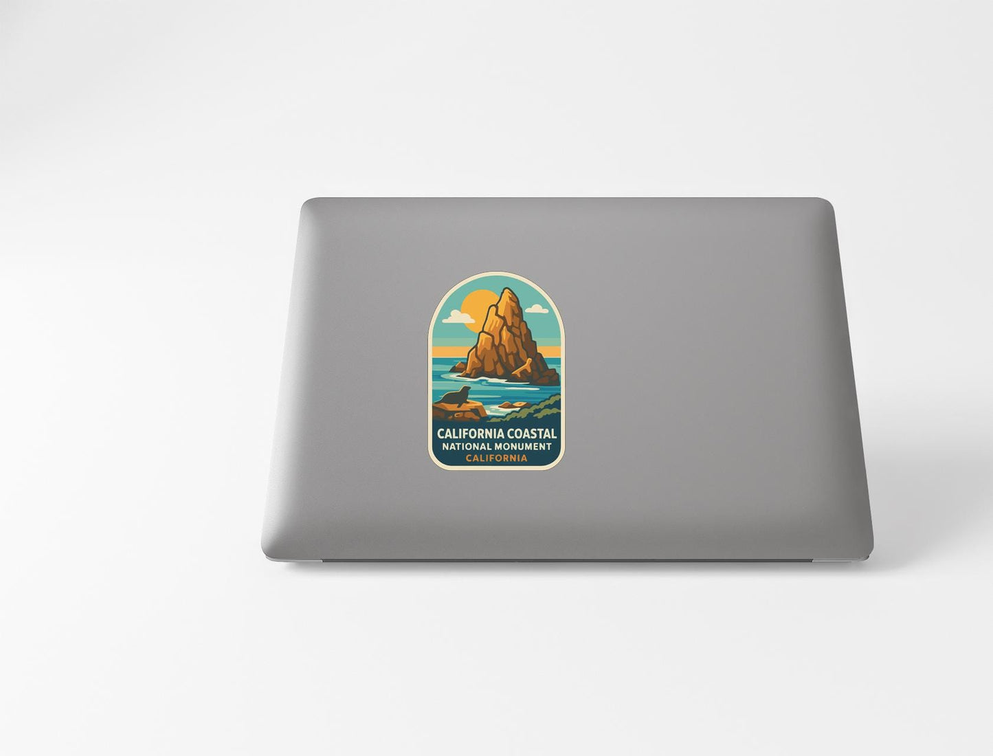 a sticker on the back of a laptop that depicts a scenic coastal landscape with mountains, water, and a sunset.