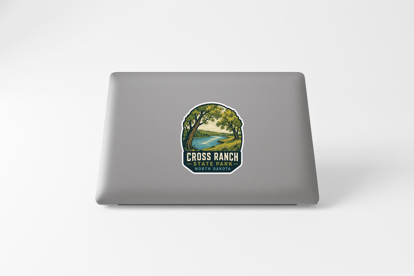 a sticker on the back of a laptop that displays a scenic landscape with a river and trees.