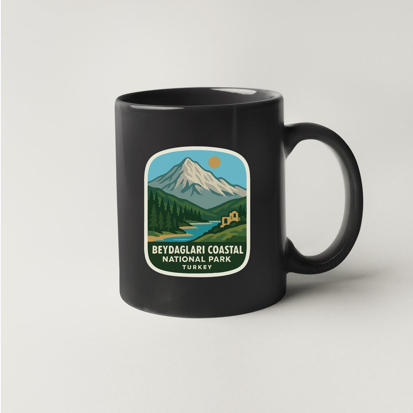 A black coffee mug with a sticker depicting a mountainous landscape and a river.