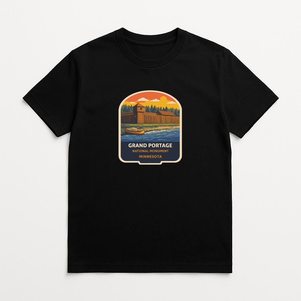 A black t-shirt with a graphic design depicting a scenic landscape featuring a castle or fortification, surrounded by trees and a body of water.
