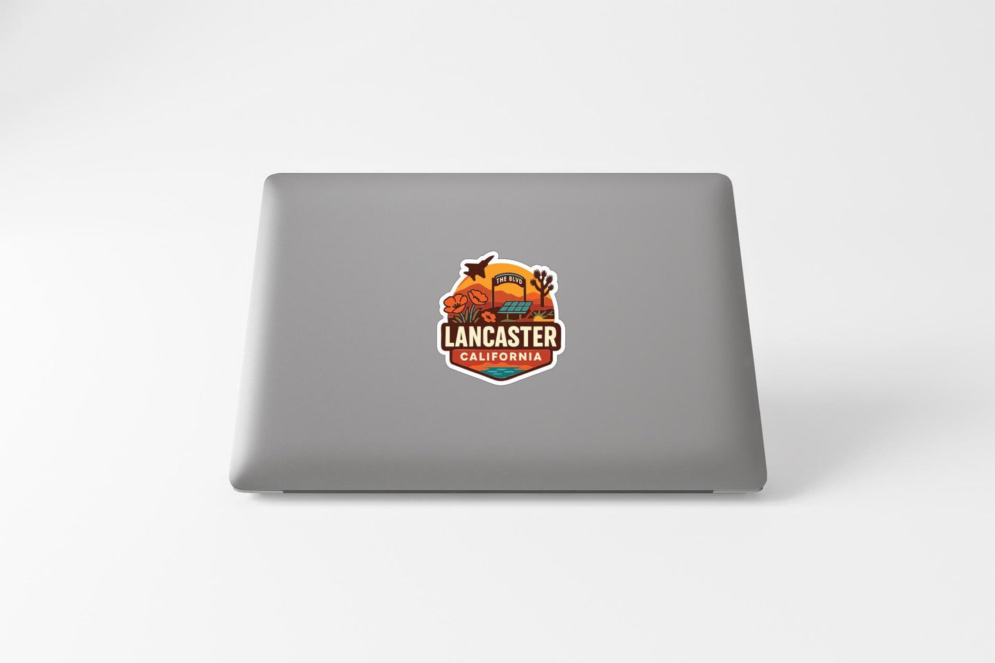 a sticker with a graphic of a desert landscape and the text "LANCASTER CALIFORNIA" on the back of a laptop.