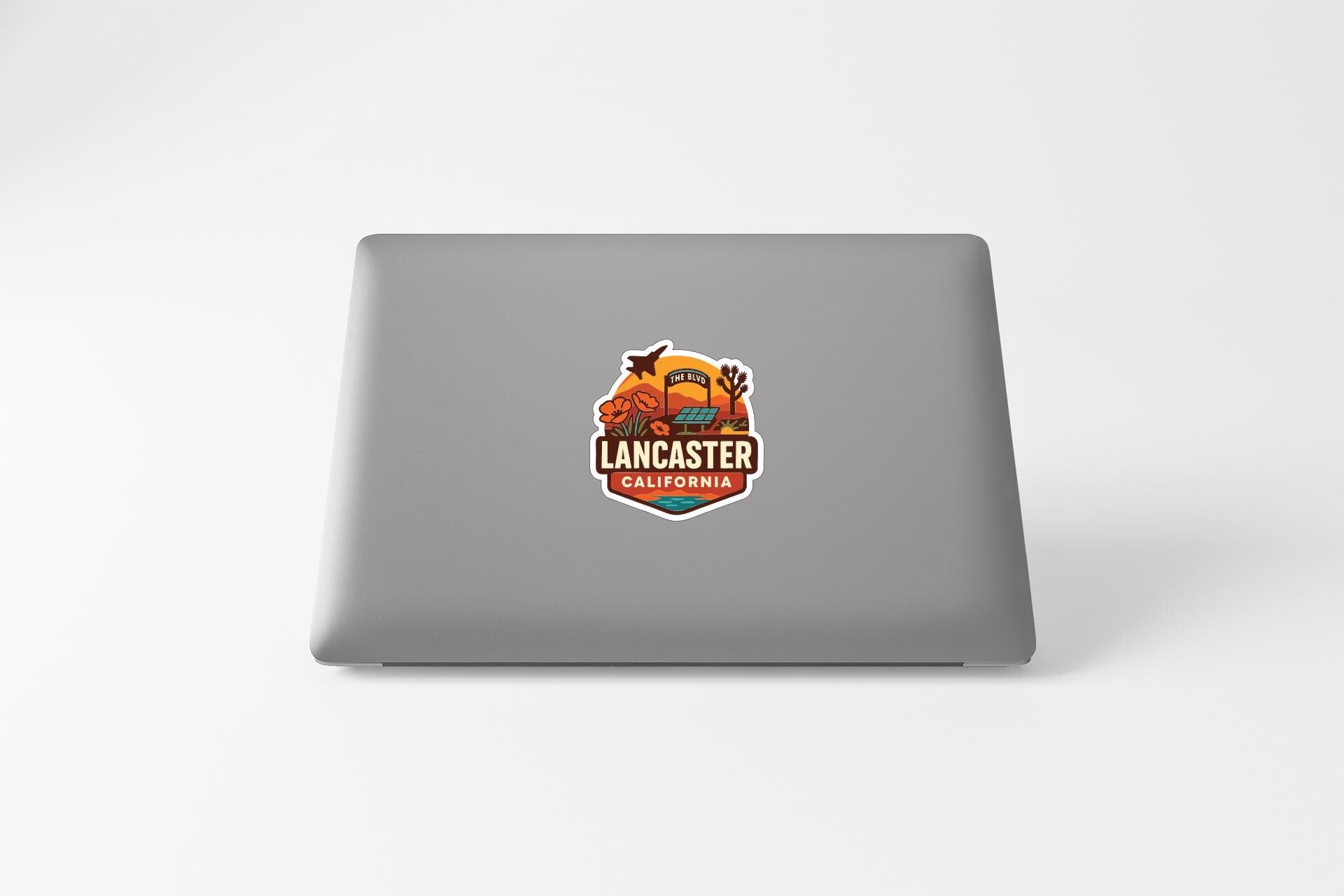 a sticker with a graphic of a desert landscape and the text "LANCASTER CALIFORNIA" on the back of a laptop.