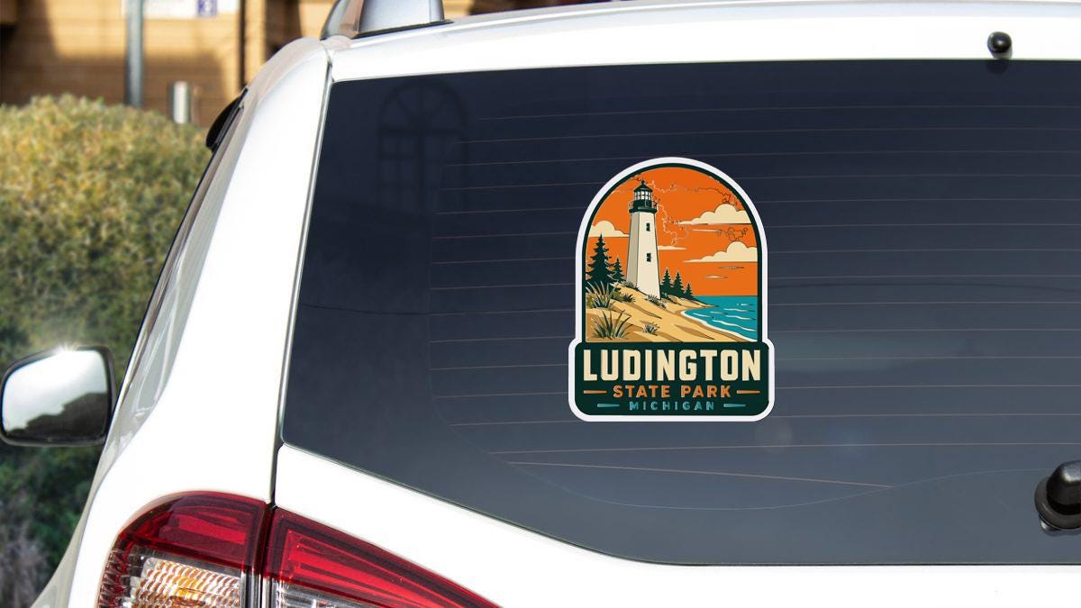 A sticker on the rear window of a white car, depicting a lighthouse and a scenic landscape.