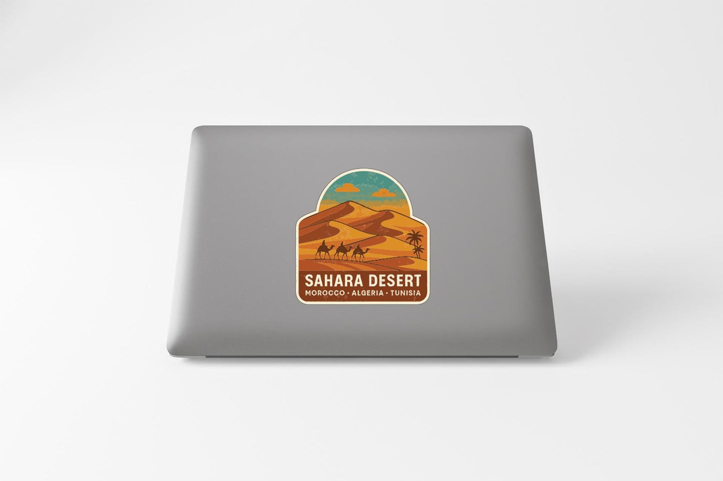 a sticker or decal on the back of a laptop, depicting a desert landscape with sand dunes and a camel.