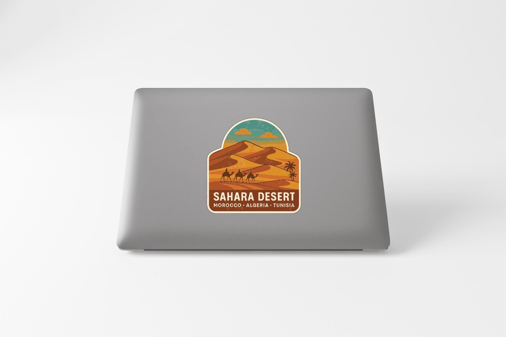 a sticker or decal on the back of a laptop, depicting a desert landscape with sand dunes and a camel.