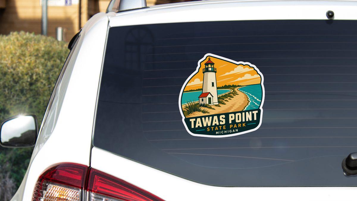 A sticker on the rear window of a car, depicting a lighthouse and a beach scene, with the text "Tawas Point State Park, Michigan".