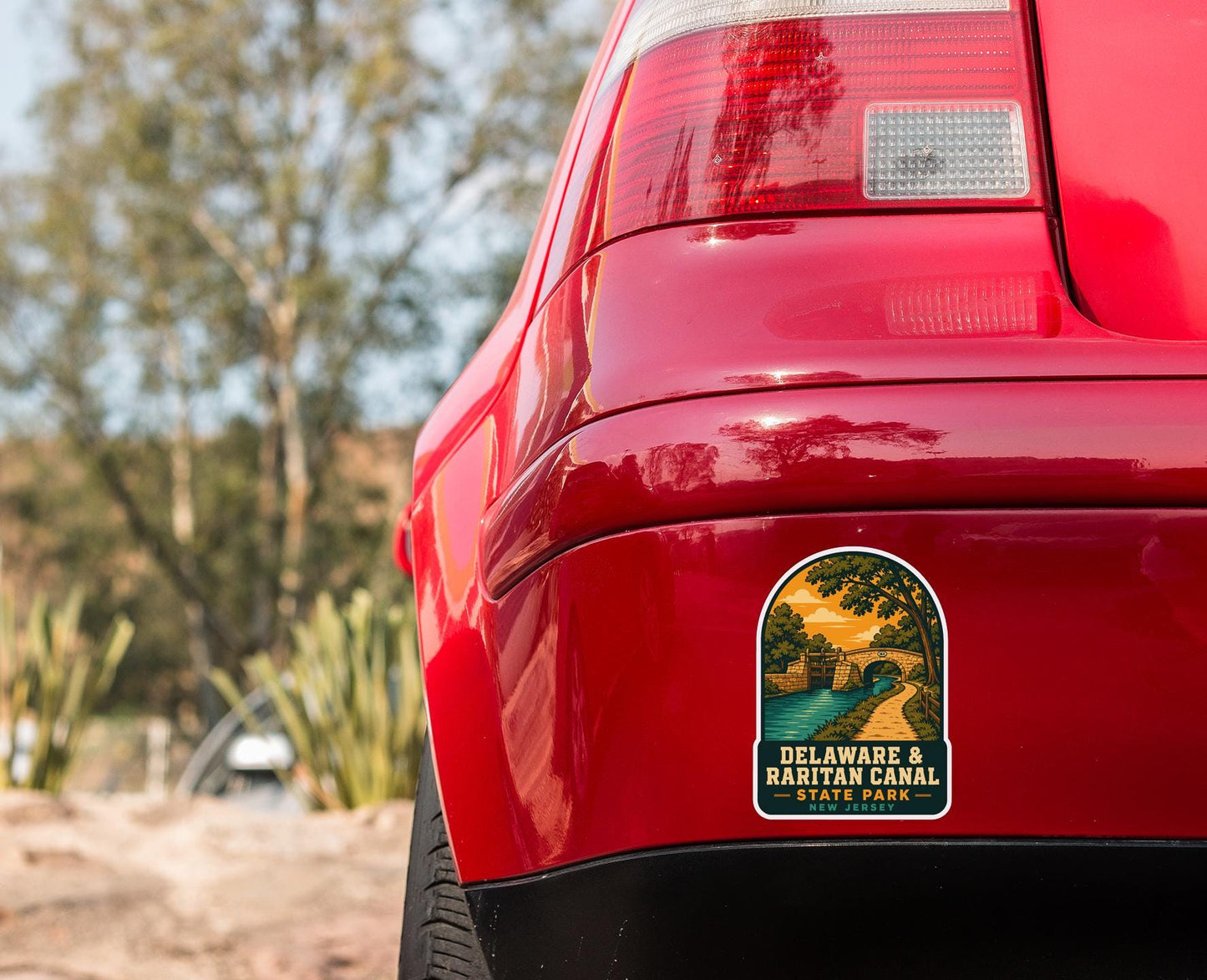 the rear end of a red car with a sticker on the trunk that says "Delaware & Racitan Canal New Jersey".