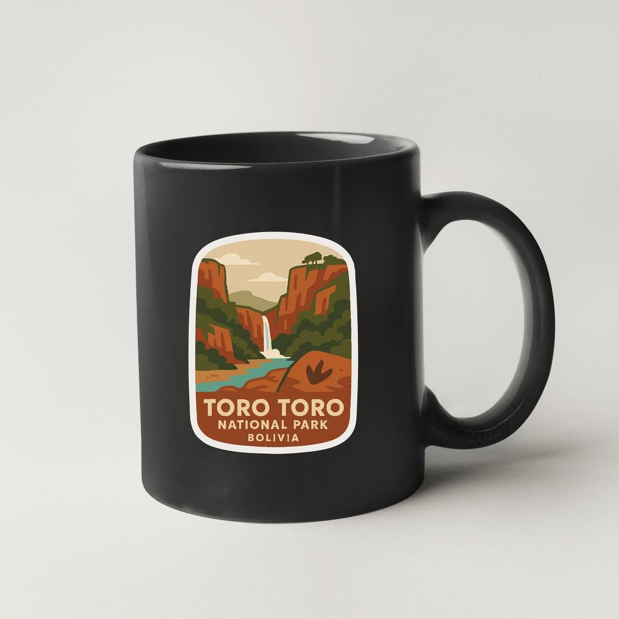A black coffee mug with a label that features a scenic mountain landscape with a waterfall and text that says "TORO TORO NATIONAL PARK BOLIVIA".