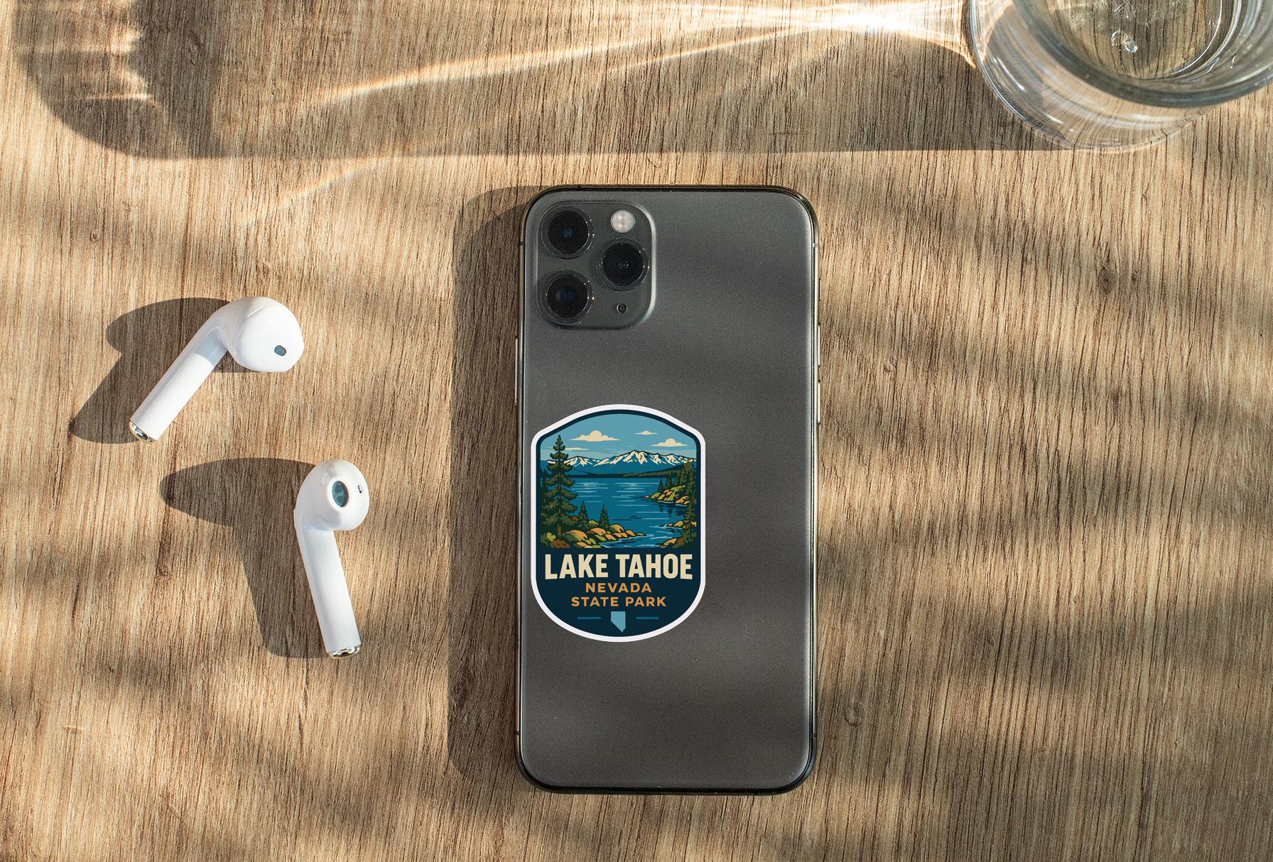 a smartphone with a sticker of Lake Tahoe, Nevada, placed on a wooden surface alongside a pair of white earbuds and a glass of water.