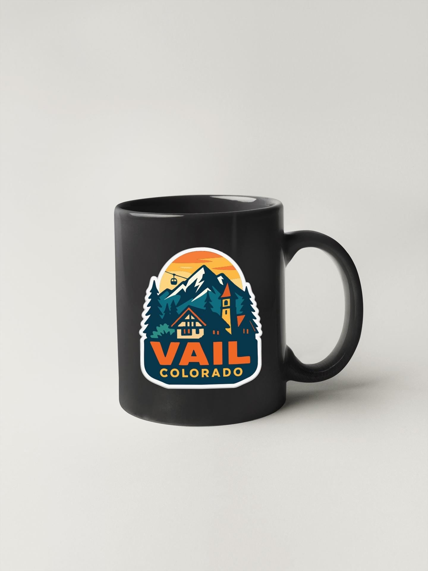 A black coffee mug with a colorful graphic design depicting a mountain landscape and the text "Vail, Colorado".
