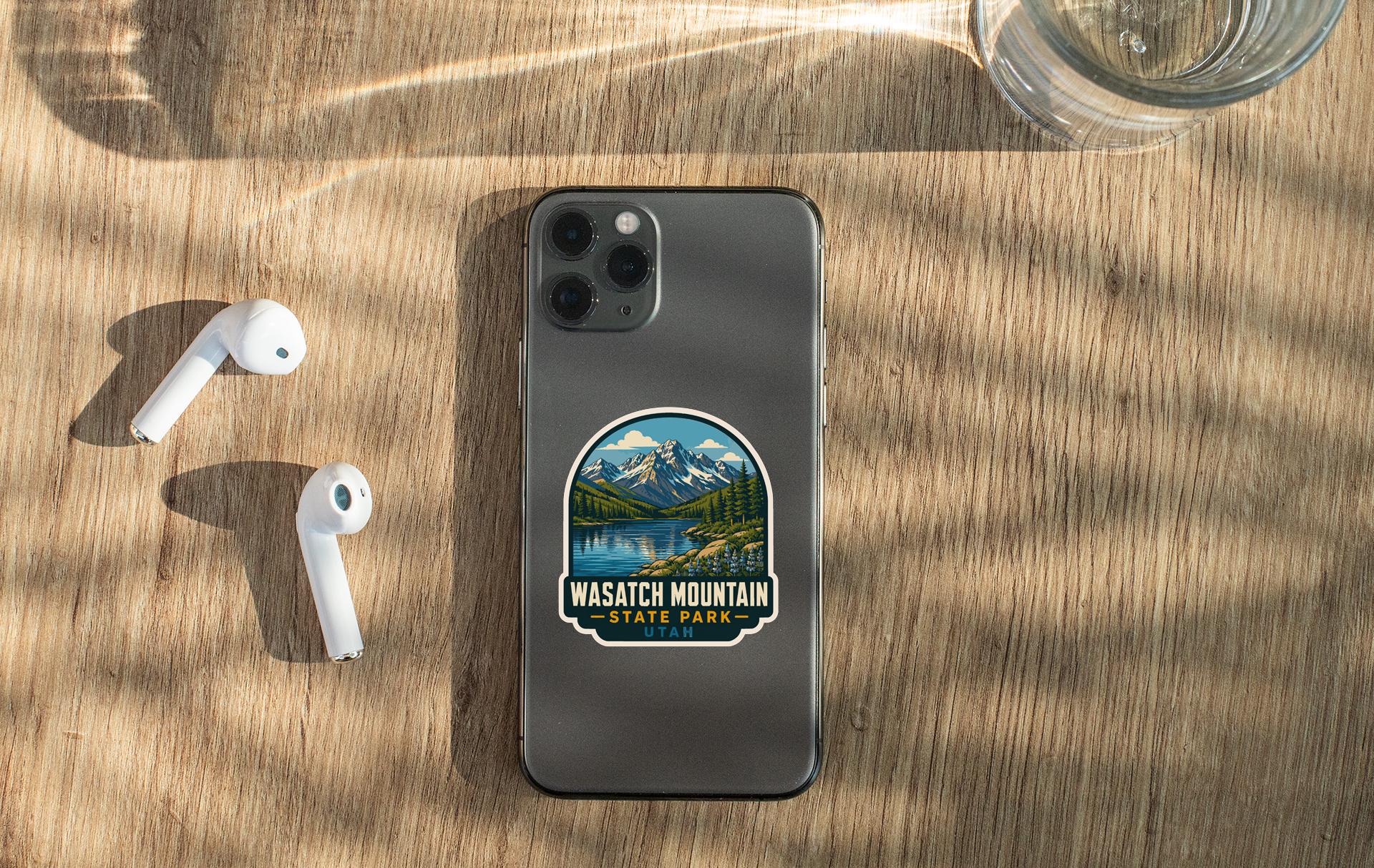 a smartphone with a sticker of Wasatch Mountain State Park on its back, along with a pair of white earbuds and a glass of water on a wooden surface.