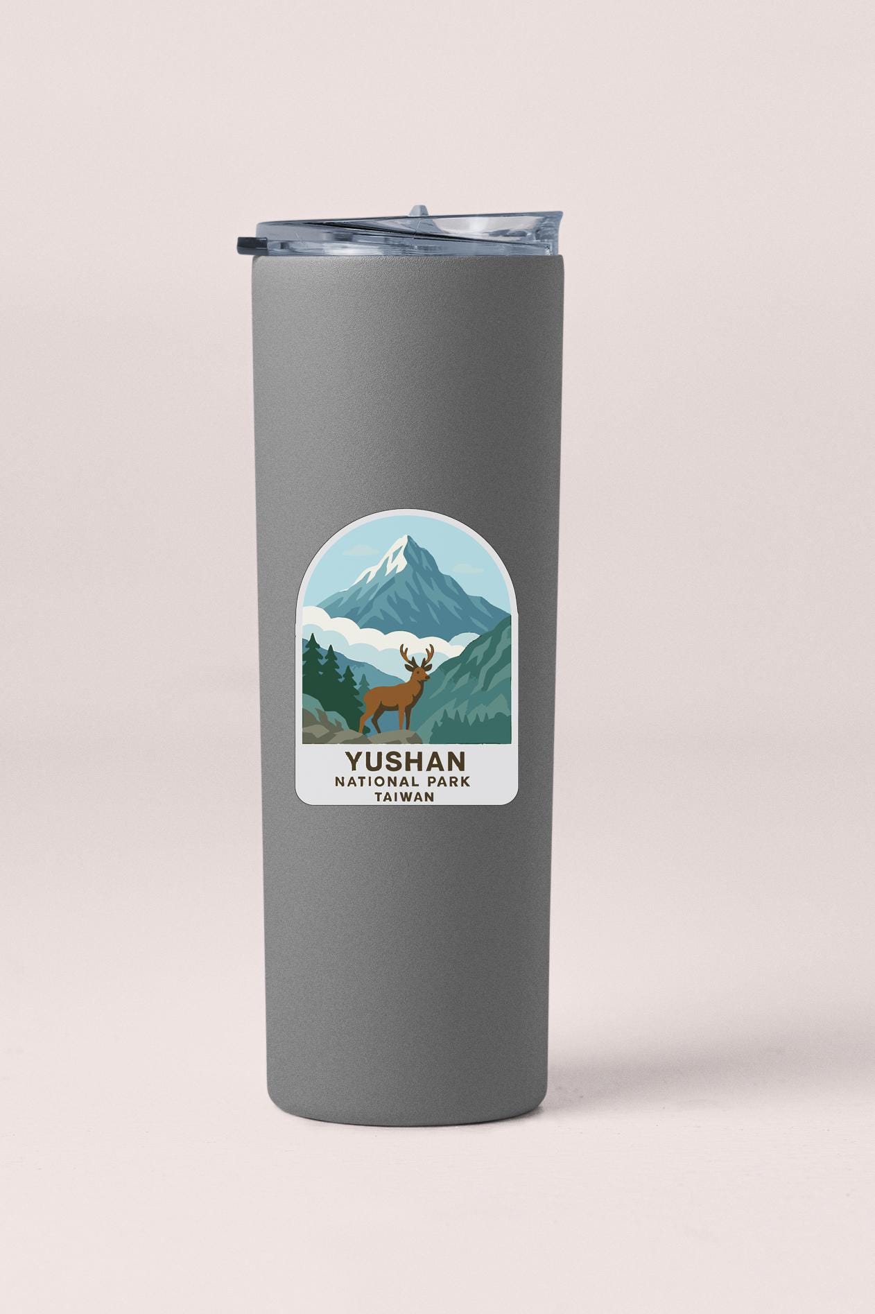 A gray tumbler with a label that features an illustration of a mountain landscape and a deer.