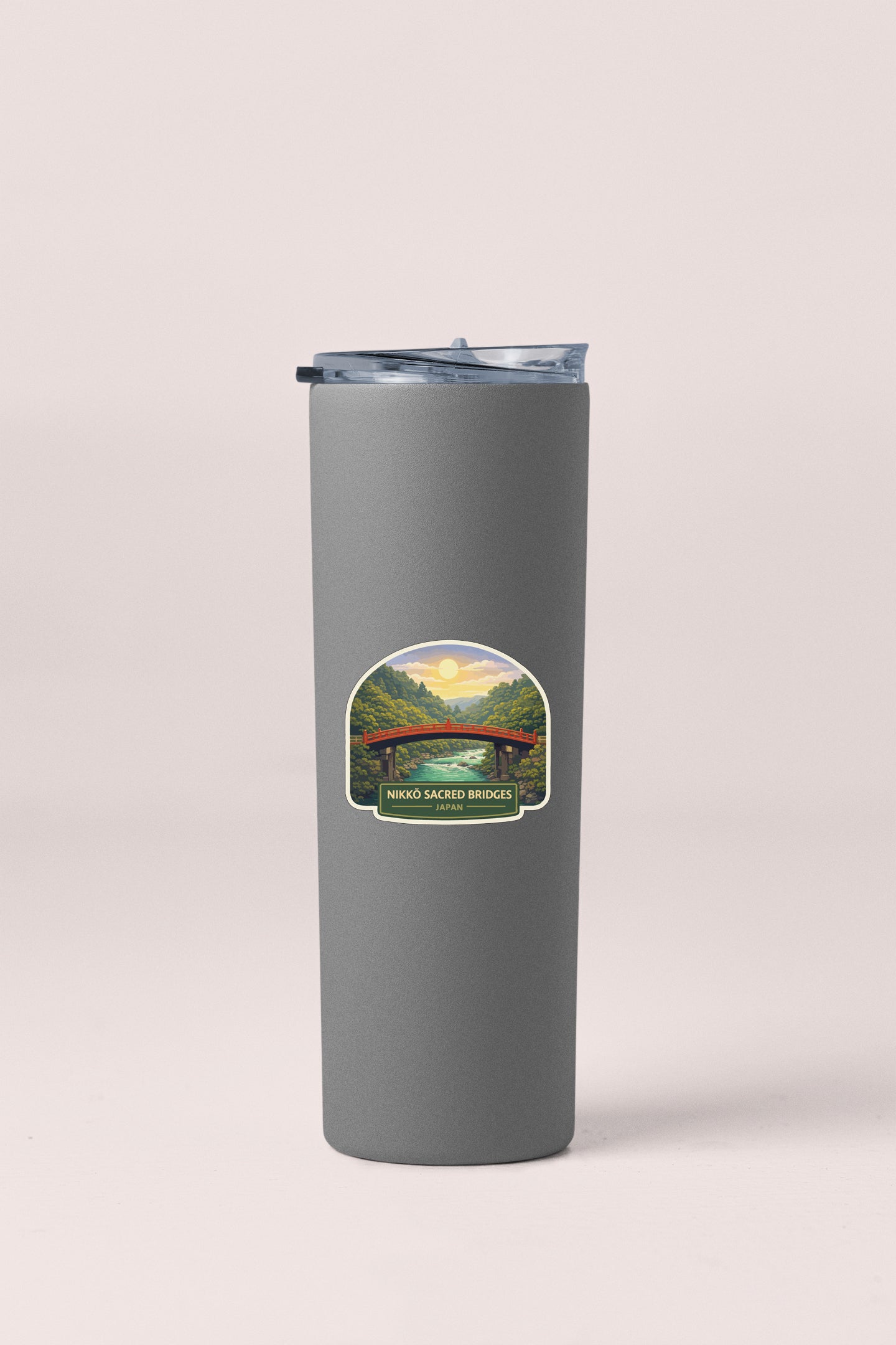 A gray insulated tumbler with a label depicting a scenic landscape featuring a bridge and a river.