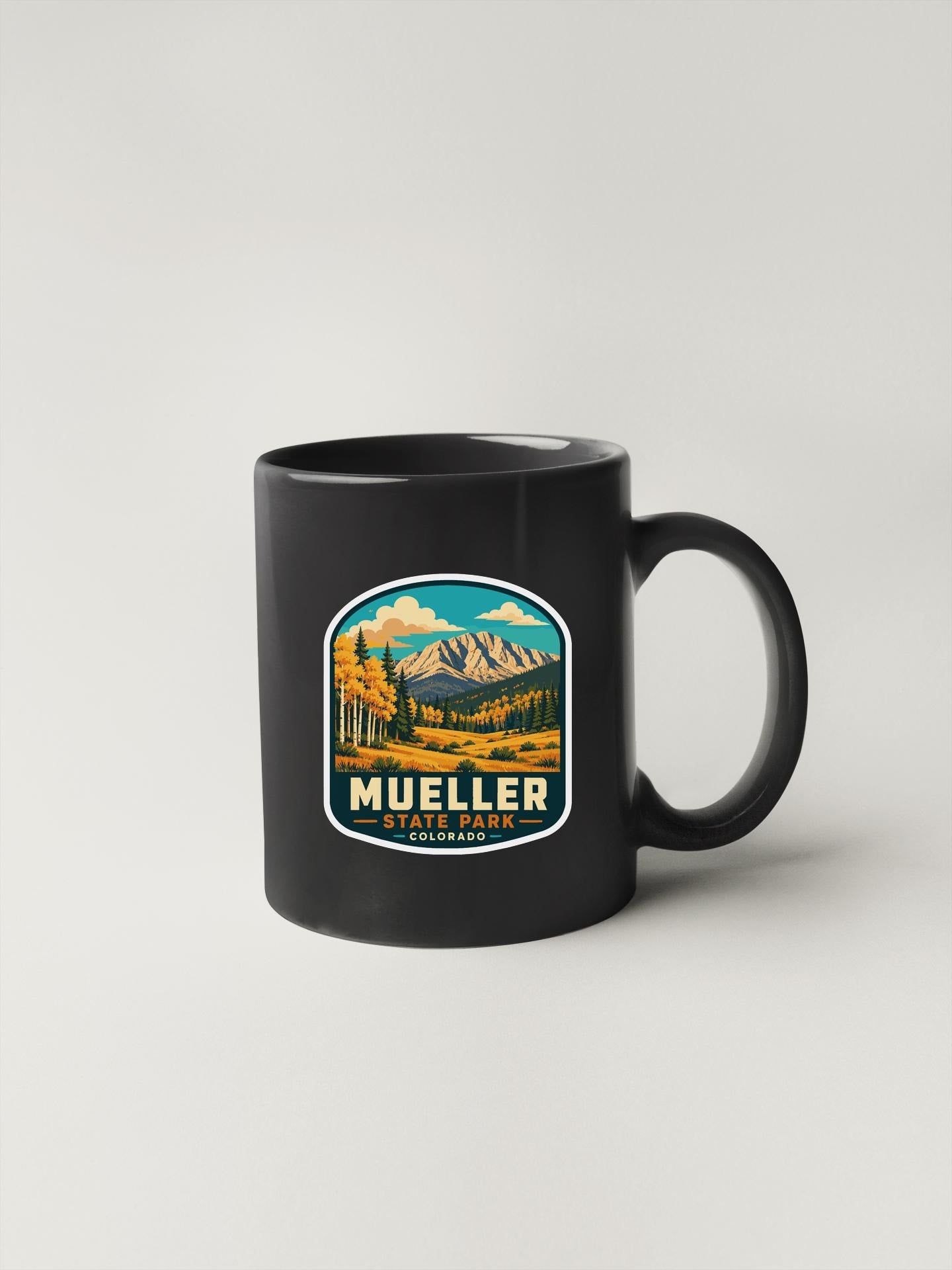 A black coffee mug with a graphic design depicting a scenic mountain landscape.