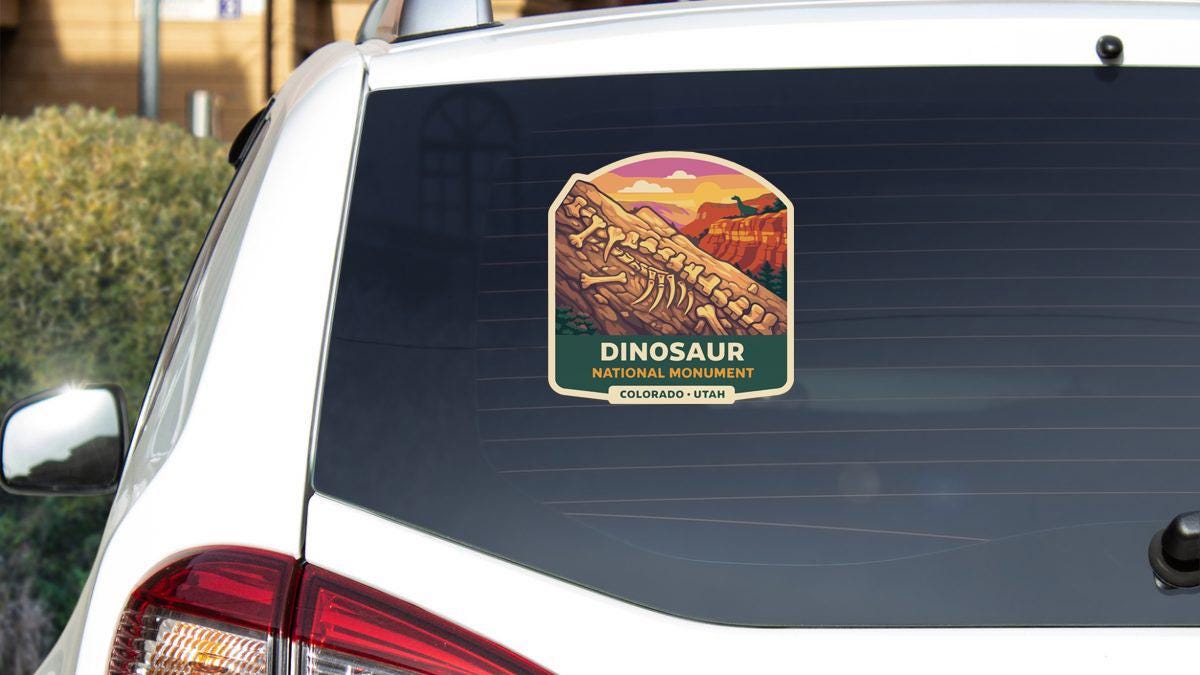 A sticker on the rear window of a white car, depicting the Dinosaur National Monument in Colorado, Utah.